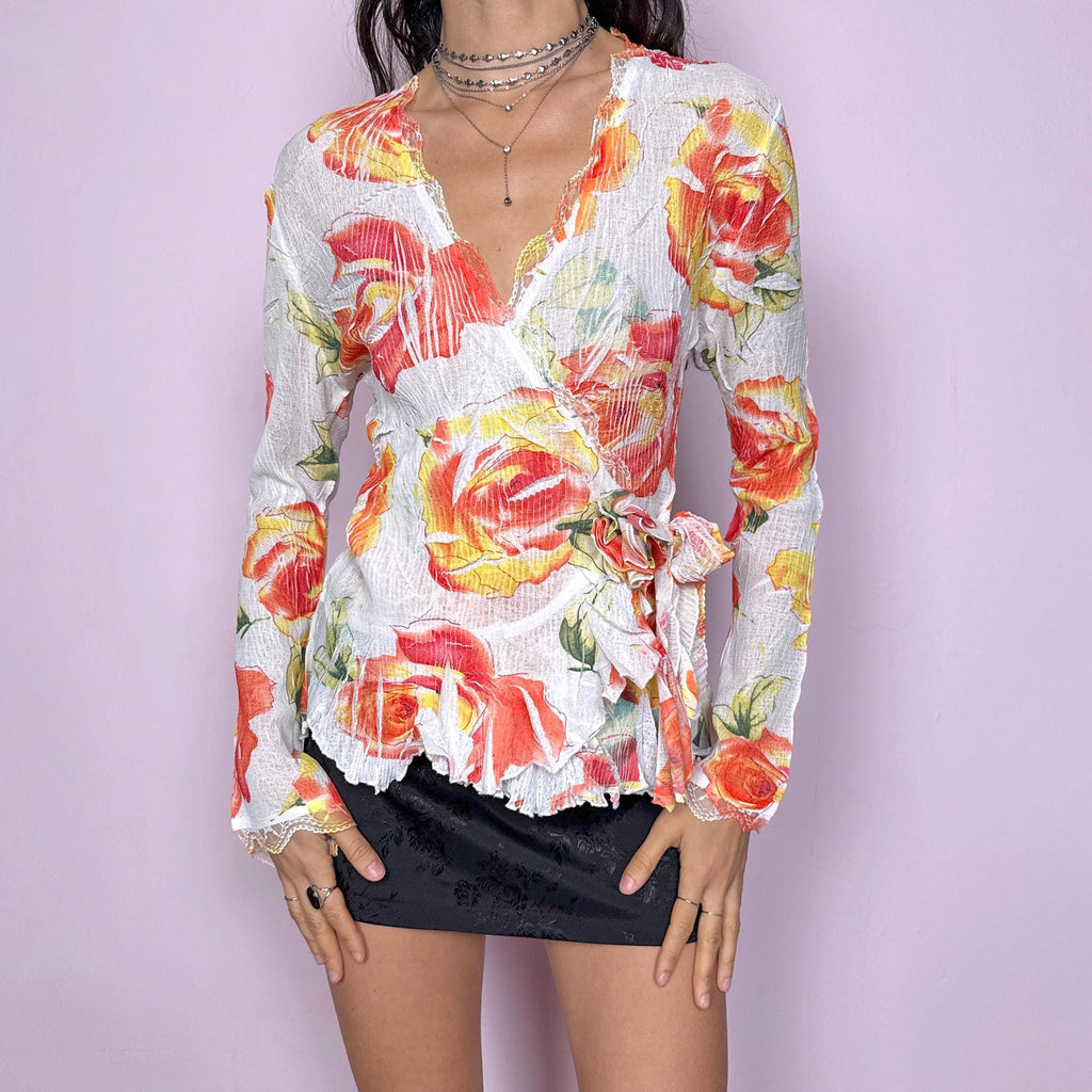 Dreamy vintage 2000s white wrap tie blouse with orange, red, and yellow rose floral print. Features lace trim, bell sleeves, crinkle pleated fabric, and rosette appliqué detail. Stunning deep V-neck top perfect for spring summer parties, formal or outdoor events. Made from stretchy polyester by a French brand. Excellent vintage condition.