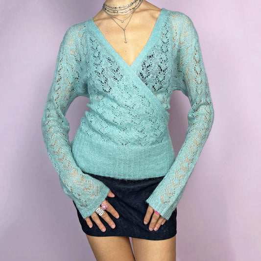 The Y2K Blue Wrap Tie Cardigan is a soft and delicate vintage 2000s piece perfect for layering. Made from a cozy open-knit sheer fabric in a dreamy pastel blue, this cardigan features a wrap-style front with a fitted waist and long sleeves. Perfect choice for transitional seasons. Excellent vintage condition.