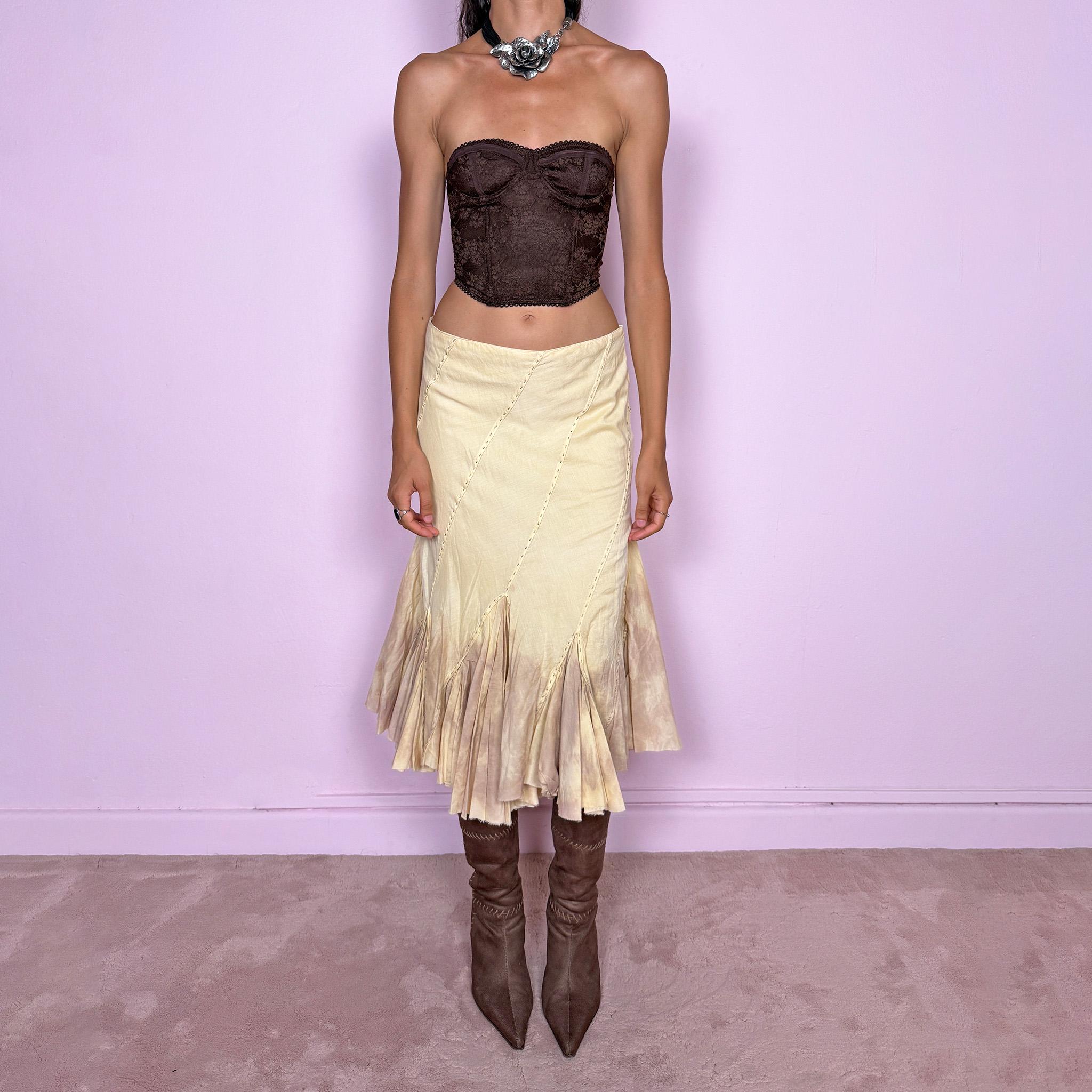 Vintage 2000s light yellow asymmetric midi skirt with a romantic, deconstructed silhouette, featuring curved diagonal paneling, visible contrast stitching, and flared godet inserts. Finished with a tie-dye effect concentrated around the lower panels and raw hem. Non-stretch fabric with a side zip closure. Can be worn mid-rise for size S or lower-rise for size XS. Ideal for bohemian, fairy-inspired, earthy, rustic, and organic summer styling.