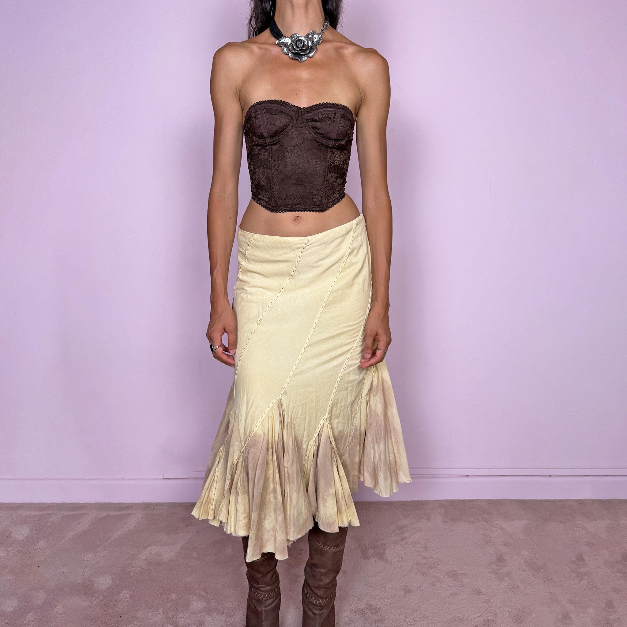 Vintage 2000s light yellow asymmetric midi skirt with a romantic, deconstructed silhouette, featuring curved diagonal paneling, visible contrast stitching, and flared godet inserts. Finished with a tie-dye effect concentrated around the lower panels and raw hem. Non-stretch fabric with a side zip closure. Can be worn mid-rise for size S or lower-rise for size XS. Ideal for bohemian, fairy-inspired, earthy, rustic, and organic summer styling.
