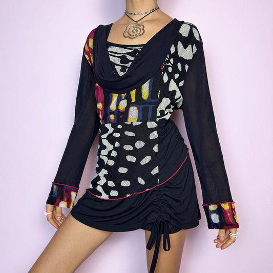 The Y2K Abstract Cowl Neck Top is a vintage 2000s rare black top featuring a vibrant abstract mixed print in bold tones. Designed with a soft cowl neckline, sheer mesh long sleeves, and contrast red stitching for an edgy finish. The ruched hemline adds shape and dimension, while the stretchy fabric keeps it comfortable. A standout piece perfect for festival looks, cybercore styling, and avant-garde deconstructed outfits. Great vintage condition. adult world shop