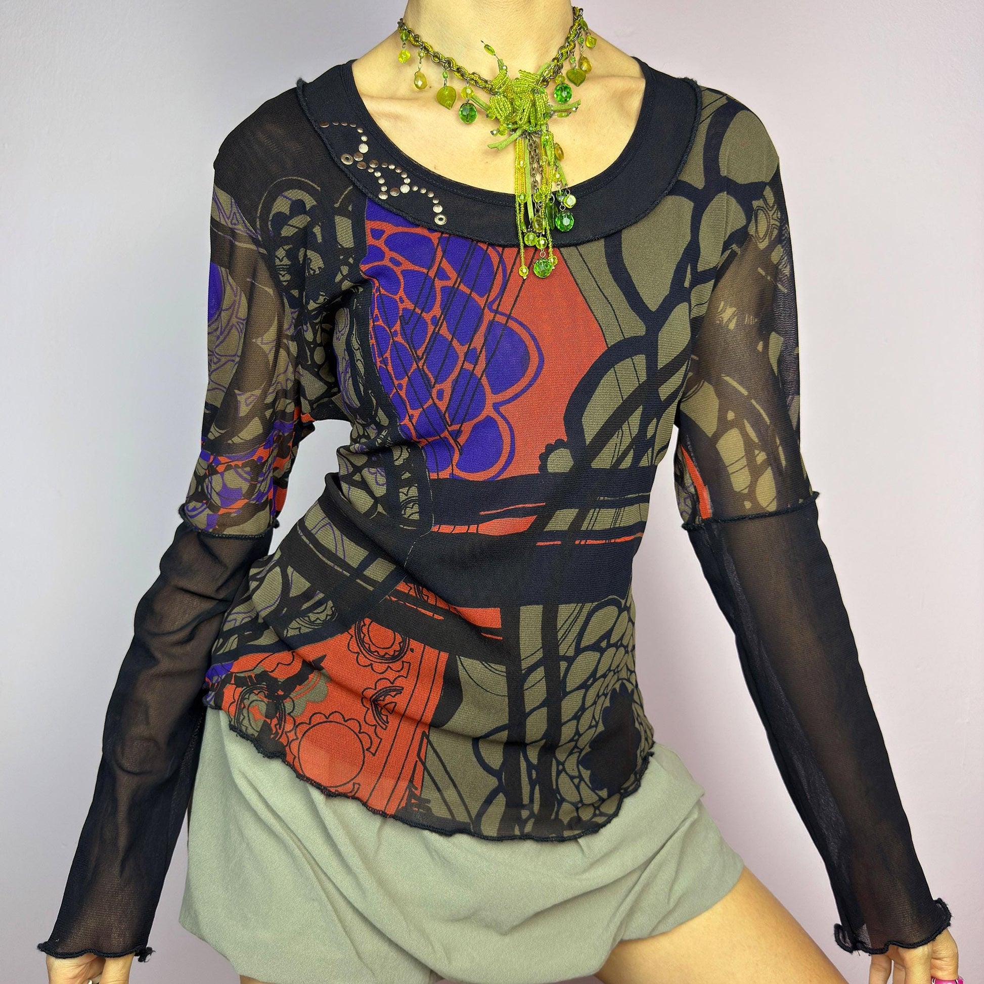 The Y2K Abstract Printed Mesh Top is a vintage 2000s sheer long-sleeve top featuring a bold abstract print in earthy tones with pops of red and blue. Designed with contrast black mesh sleeves, this artistic piece is perfect for edgy streetwear, cyberpunk, or grunge-inspired outfits. Ideal for layering or wearing solo for a statement look. adult world shop