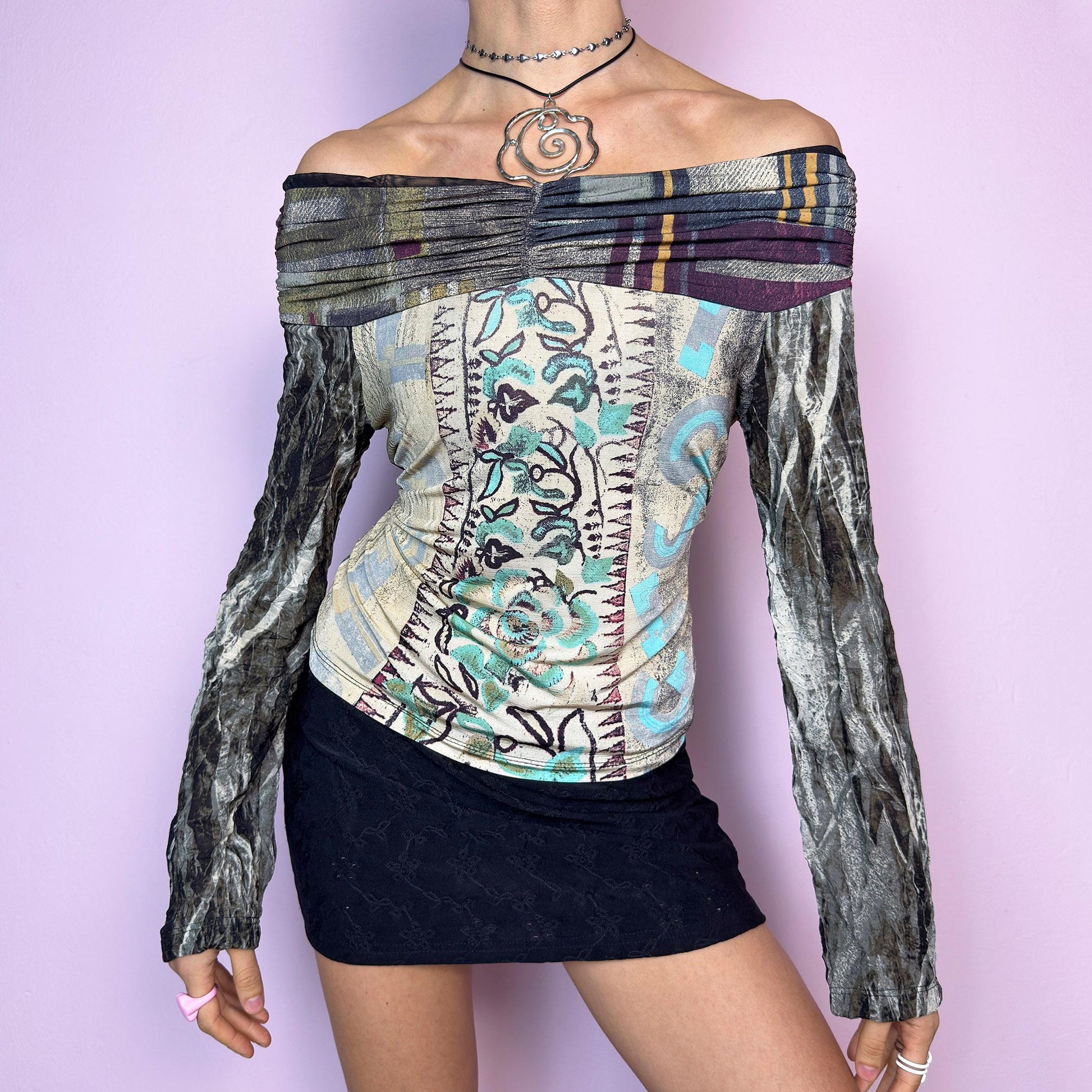 The Y2K Art Print Top is a vintage 2000s off-the-shoulder long sleeve designed by Legatte Jeans. This artsy piece features a unique patchwork-style mixed print with floral, stripe, and abstract motifs in a moody palette of cream, sage, burgundy, and metallic gray. The body is made from soft, stretchy fabric, while the semi-sheer mesh sleeves add a delicate contrast. Pleated details along the neckline elevate its sculptural silhouette. adult world shop