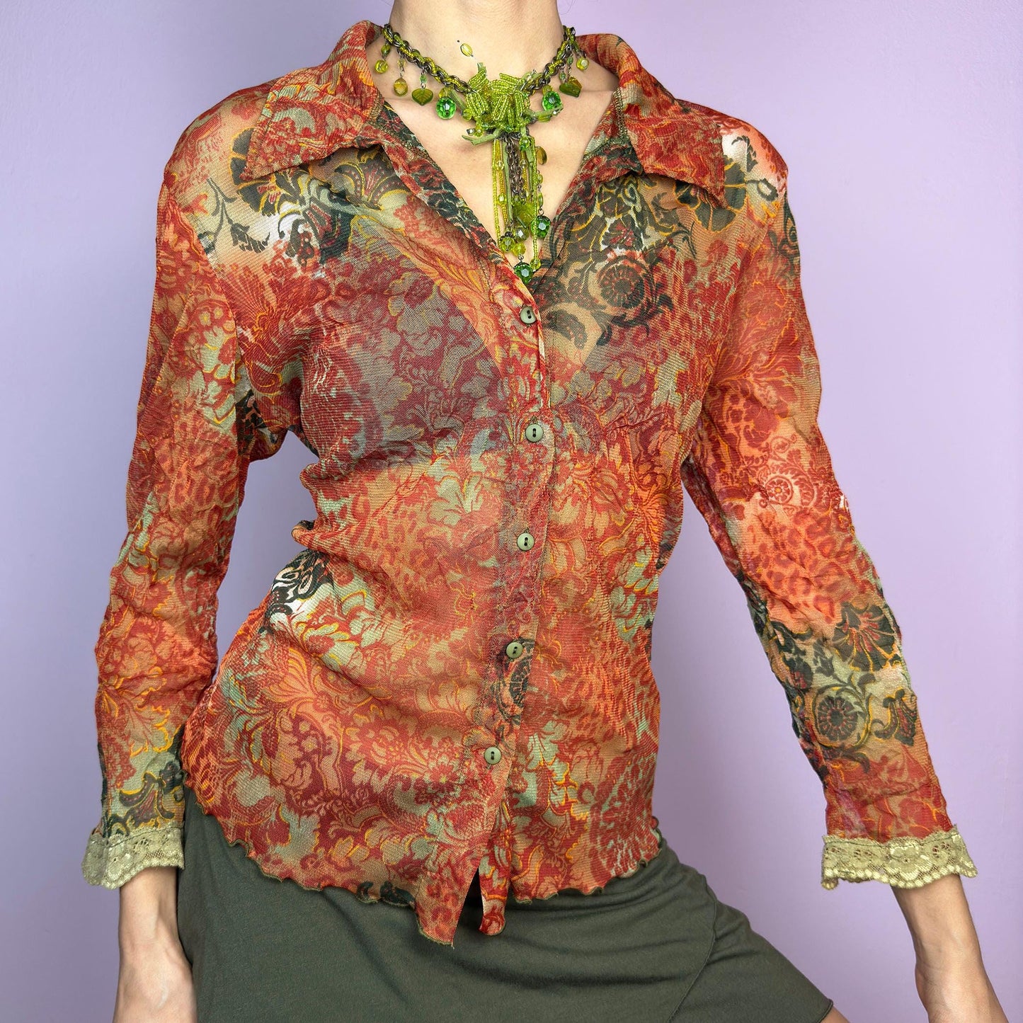 The Y2K Baroque Print Mesh Blouse is a vintage 2000s piece featuring a semi-sheer mesh fabric with a rich baroque-inspired floral print in warm tones. Designed with a fitted silhouette, button-up front, delicate lace trim on the cuffs and three quarter sleeves, the lightweight and stretchy fabric make it ideal for summer bohemian-inspired looks. adult world shop