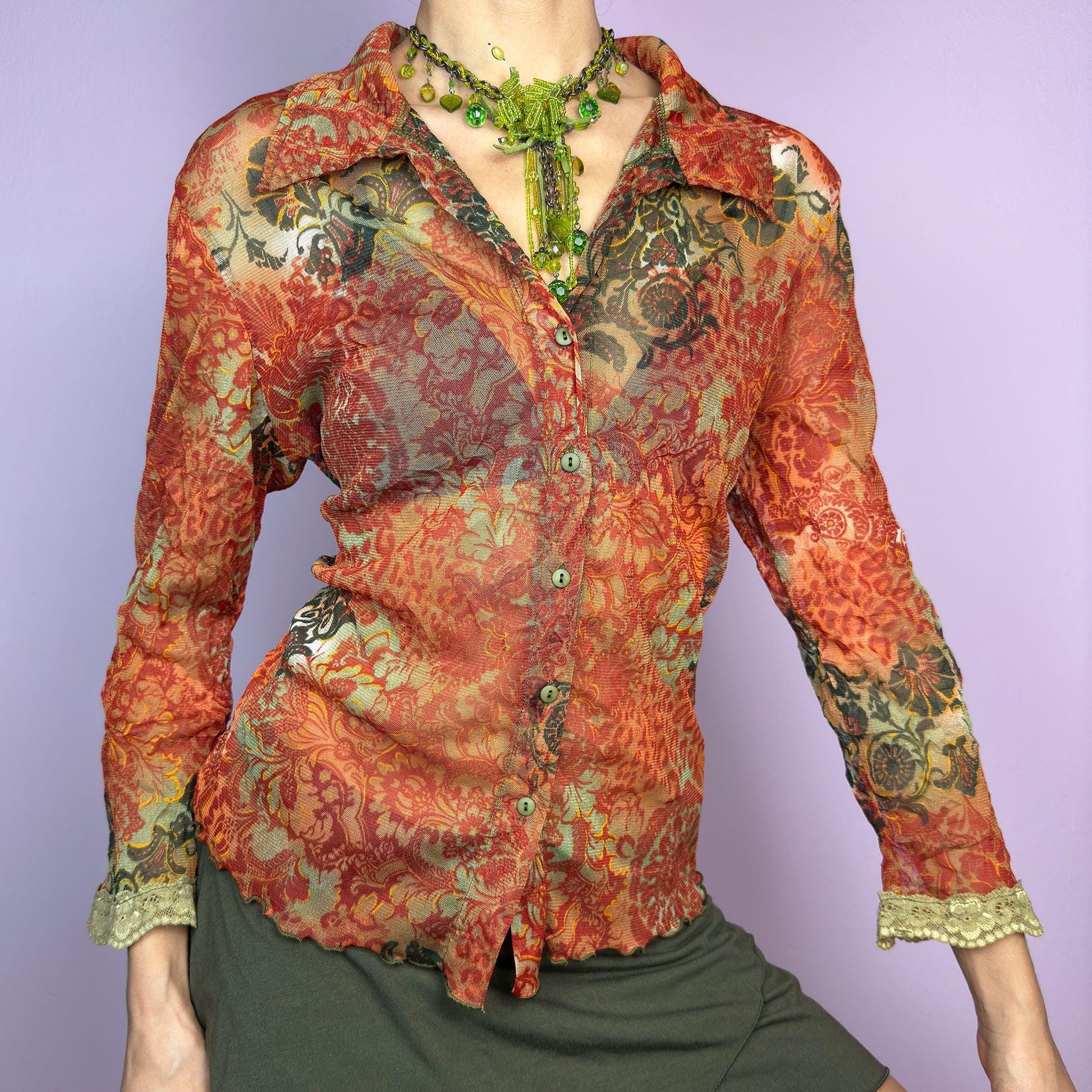 The Y2K Baroque Print Mesh Blouse is a vintage 2000s piece featuring a semi-sheer mesh fabric with a rich baroque-inspired floral print in warm tones. Designed with a fitted silhouette, button-up front, delicate lace trim on the cuffs and three quarter sleeves, the lightweight and stretchy fabric make it ideal for summer bohemian-inspired looks. adult world shop