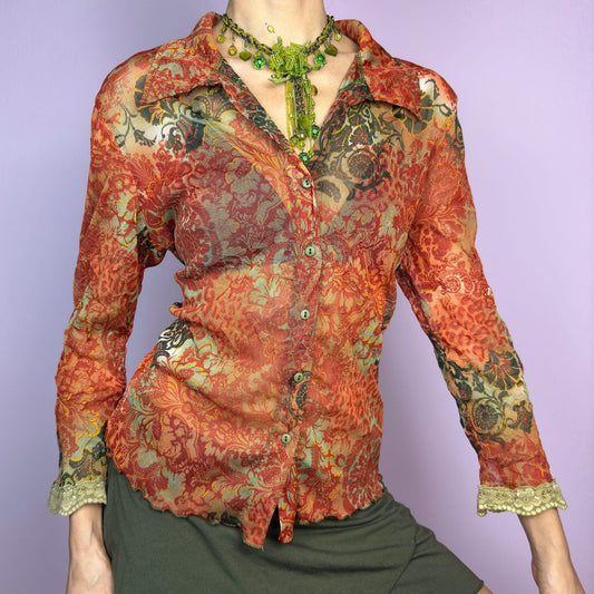 The Y2K Baroque Print Mesh Blouse is a vintage 2000s piece featuring a semi-sheer mesh fabric with a rich baroque-inspired floral print in warm tones. Designed with a fitted silhouette, button-up front, delicate lace trim on the cuffs and three quarter sleeves, the lightweight and stretchy fabric make it ideal for summer bohemian-inspired looks. adult world shop