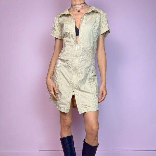 The Y2K Beige Zip-Up Mini Dress is a vintage 2000s utilitarian dress. Crafted in a lightweight, parachute-style fabric, it features a full front zip closure, fold-over collar, short sleeves, and side pockets. The fitted silhouette and double zipper let you play with styling—unzipped for attitude, zipped up for sleek utility. Perfect for techwear, streetwear, or minimalist work looks. Great vintage condition.