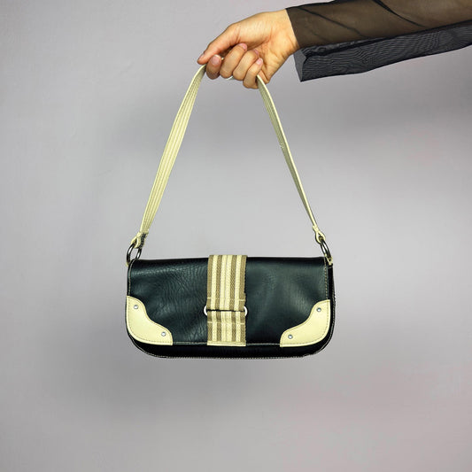 The Y2K Black Baguette Shoulder Bag is a sleek and compact vintage 2000s piece featuring a black faux leather exterior with contrasting cream accents and a striped strap detail. Designed with a zipper pocket at the back. adult world shop