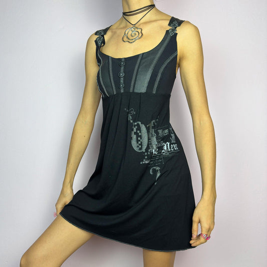 The Y2K Black Buckle Strap Mini Dress is a vintage 2000s sleeveless piece with a mix of edgy and casual aesthetics. It features decorative button details, contrast stitching, and graphic prints. adult world shop