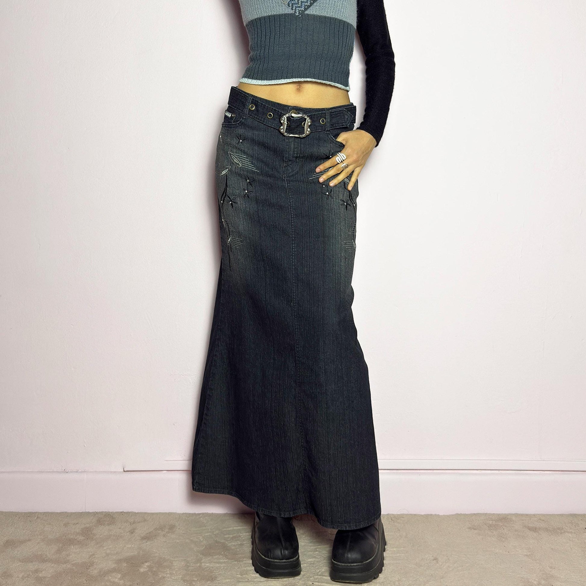The Y2K Black Denim Maxi Skirt is a vintage 2000s piece featuring a sleek dark wash, rhinestone embellishments, and contrast stitching. Designed with a mid-rise fit and a stretchy denim fabric, it offers a structured silhouette that flares at the bottom. The skirt is finished with a button and zipper closure, pockets, and a removable belt for a customizable look. Perfect for casual streetwear outfits or an elegant night out. adult world shop