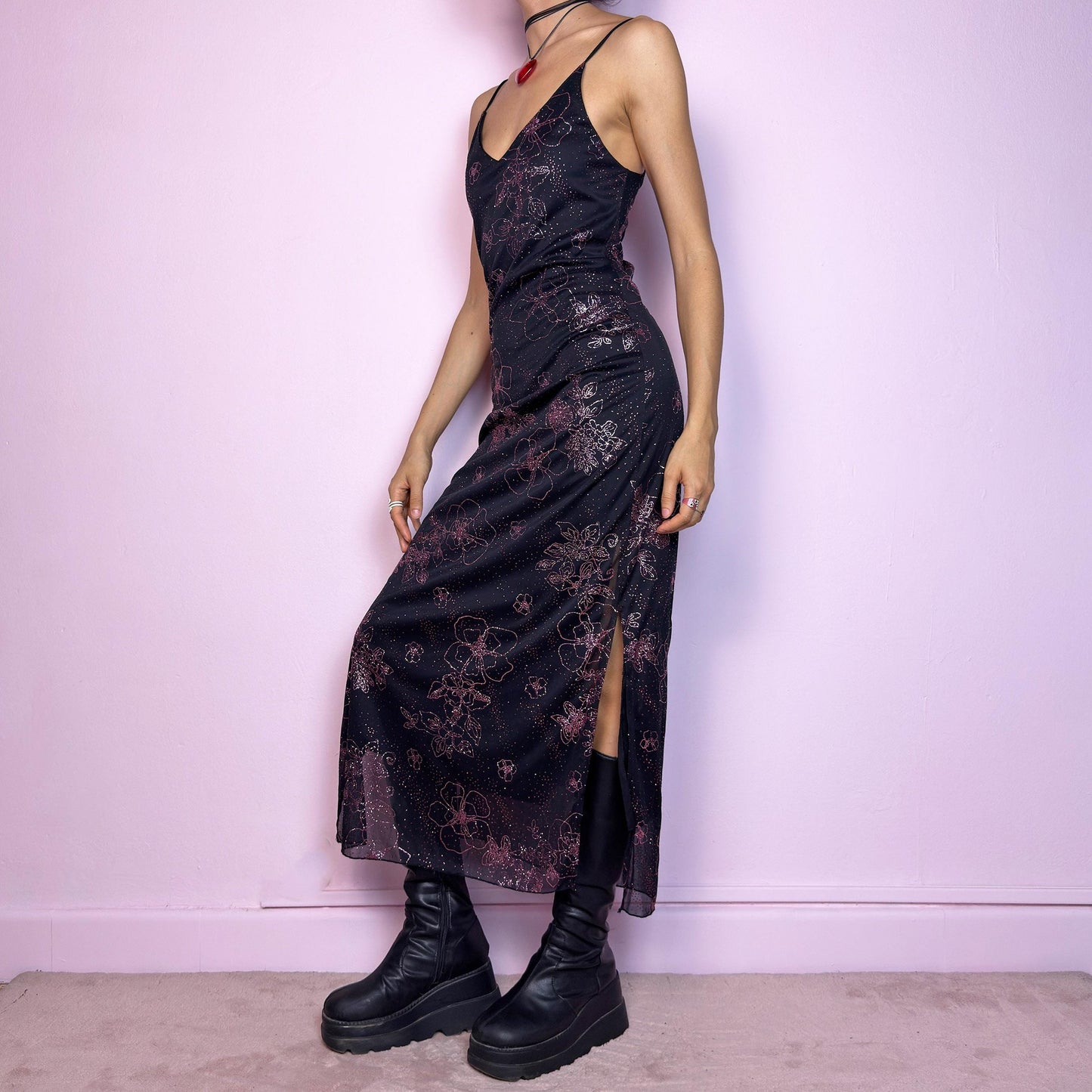 The Y2K Black Glitter Midi Dress is a rare 2000s dress featuring a delicate pink glitter floral pattern on a sheer black mesh overlay with a soft lining beneath. This midi-length piece includes skinny spaghetti straps, a deep V neckline, and a side slits for added movement. The open lace-up back detail gives it a sultry edge, perfect for night outs, alt party looks, or romantic goth aesthetics. Fitted silhouette with a flattering drape. Made in France. Excellent vintage condition.