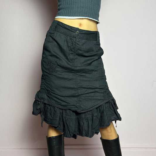 The Y2K Black Layered Skirt by Marithé François Girbaud is a vintage 2000s statement piece featuring a structured design with ruched details and ruffled layers for added texture and movement. Designed with a mid-rise fit, button and zipper closure, embroidered side detail, and an asymmetrical hem, this skirt blends edgy streetwear vibes with a playful, gothic aesthetic. Perfect for casual grunge and alternative looks. adult world shop