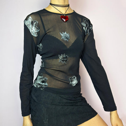 The Y2K Black Mesh Appliqué Top is a vintage 2000s sheer black mesh top featuring abstract velvet appliqués in silver tones across the front, a fitted silhouette with long sleeves and soft stretch fabric. Eye-catching and edgy – ideal for layering, night out looks, or styled as rave, grunge, or clubwear. Great vintage condition. adult world shop