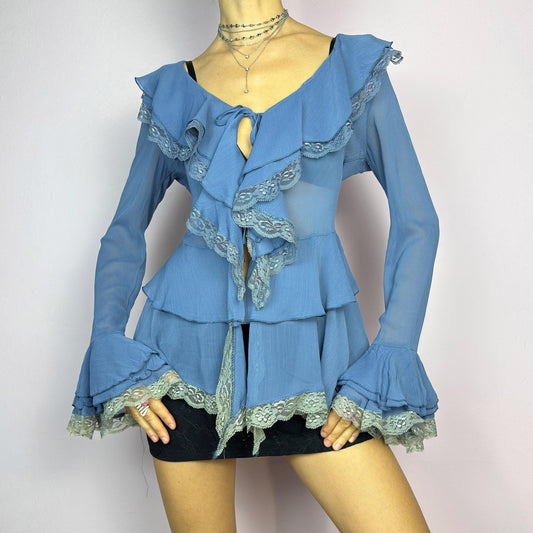 The Y2K Blue Ruffle Blouse is a dreamy vintage 2000s piece with a romantic and ethereal aesthetic. Crafted from a sheer, lightweight fabric in a soft blue shade, this blouse features cascading ruffles with delicate lace trim. adult world shop