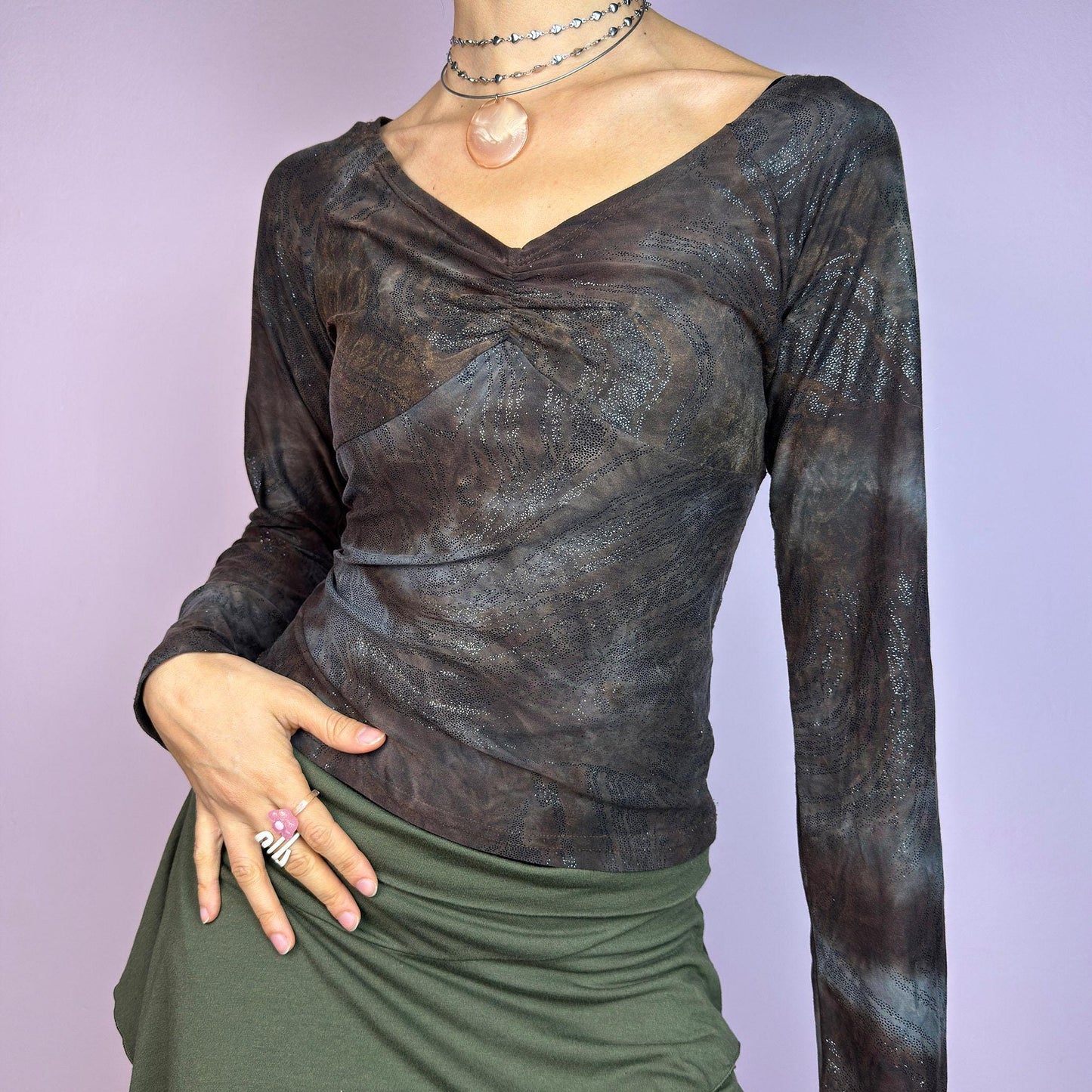 The Y2K Brown Earthy Shimmer Top is a vintage 2000s fitted and stretchy long-sleeve blouse with an earthy, abstract pattern featuring a ruched detail at the bust and subtle shimmering accents throughout. Perfect for casual outings. adult world shop