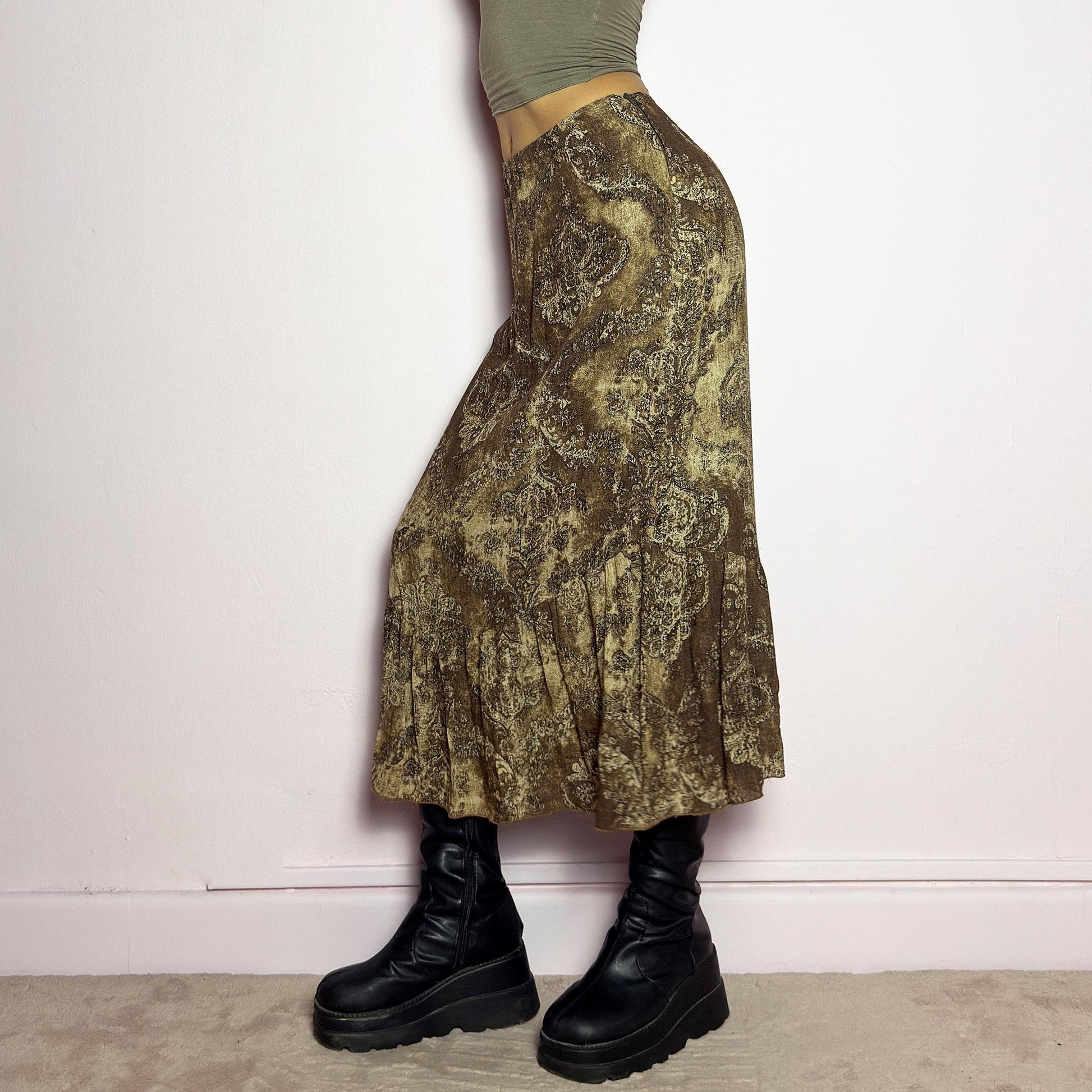 The Y2K Brown Paisley Midi Skirt is a vintage 2000s piece featuring a baroque-inspired paisley print. Designed with an earthy, whimsical aesthetic, this skirt has a flowy silhouette with subtle ruffle tiered details at the hem. It features a side zipper closure with an elastic waist. Perfect for grunge and bohemian-inspired outfits. adult world shop