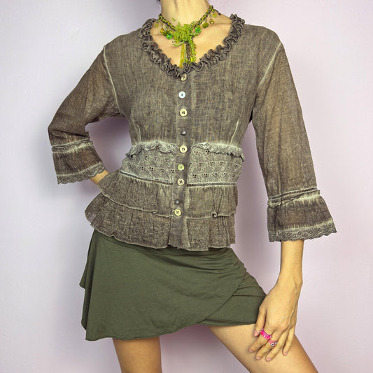 The Y2K Brown Ruffle Frill Blouse is a vintage 2000s piece featuring a faded brown wash with delicate lace trims and tiered ruffle details for a romantic, fairy-grunge aesthetic. Designed with a button-up front, 3/4 bell sleeves, this blouse blends cottagecore and bohemian elements effortlessly. The soft, lightweight fabric makes it perfect for dreamy summer outfits. adult world shop