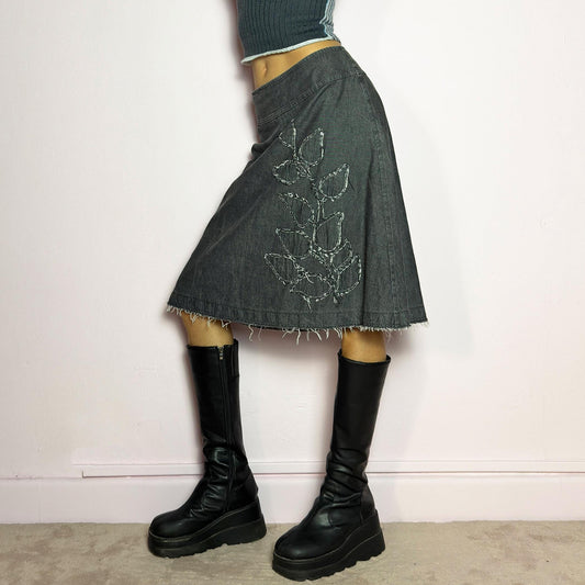 The Y2K Denim Gray Midi Skirt is a vintage 2000s piece featuring a faded gray wash, raw hem, and a unique floral sequin embroidery design. Crafted from structured denim, this skirt has an A-line silhouette that drapes effortlessly. Designed with a back zipper closure, the unfinished hem adds a deconstructed, edgy touch, making it perfect for casual outfits. adult world shop