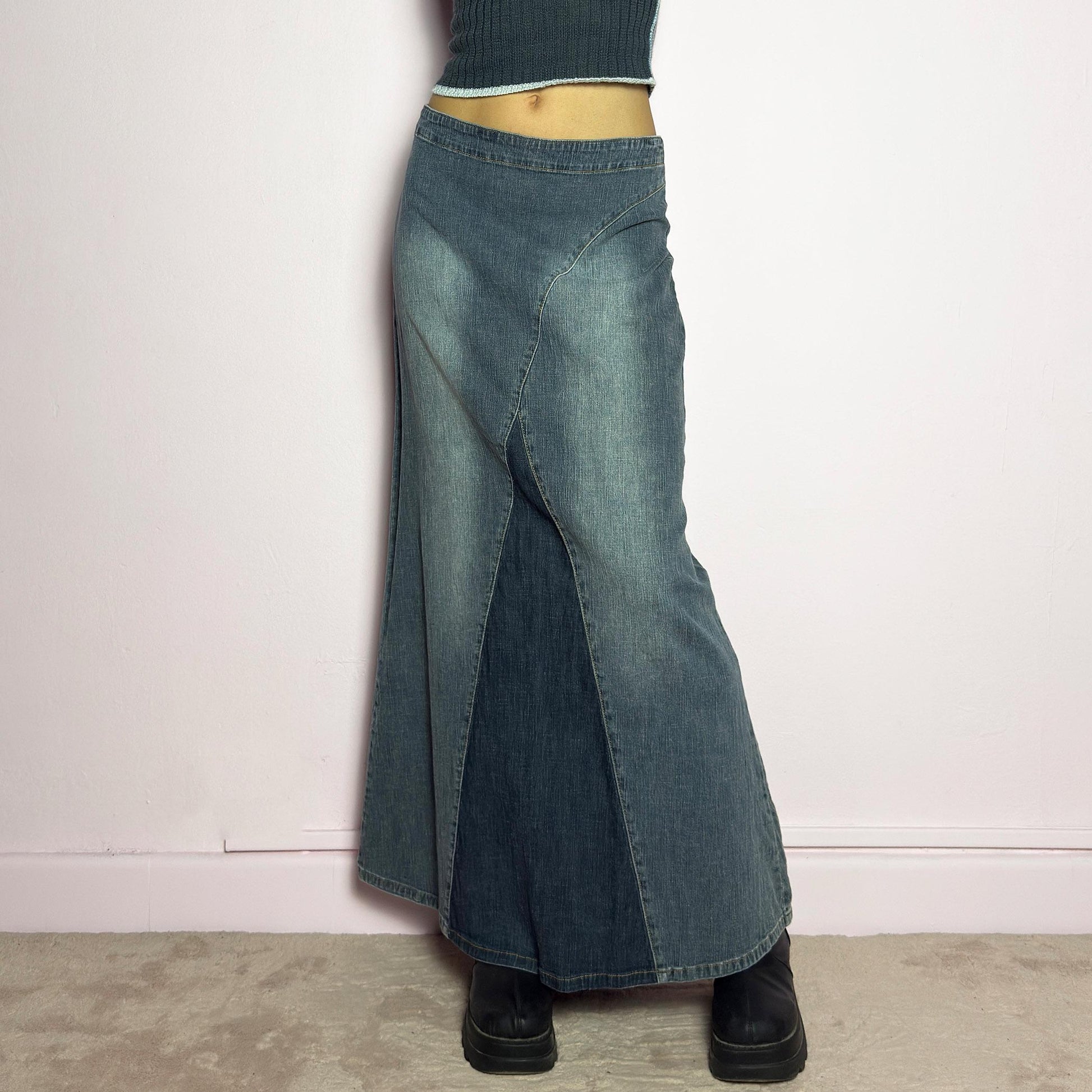 The Y2K Denim Paneled Maxi Skirt is a vintage 2000s piece featuring a unique paneled design with contrast wash details. Crafted from structured stretchy denim, this skirt offers a flattering mid-rise fit with a sleek, flared silhouette. Designed with a back zipper closure and a subtle back slit for ease of movement, it&#39;s perfect for casual streetwear outfits. adult world shop