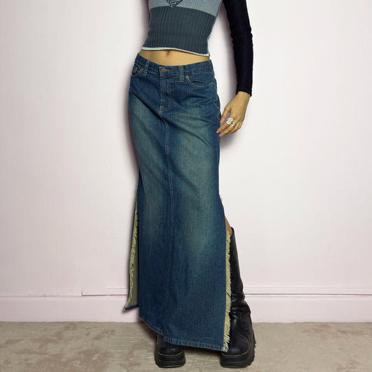 The Y2K Denim Side Slit Maxi Skirt is a vintage 2000s statement piece featuring a structured mid-rise fit and a sleek, elongated silhouette. Designed with frayed side slit details, a button and zipper closure, and classic five-pocket styling, this skirt is perfect for casual streetwear looks. adult world shop