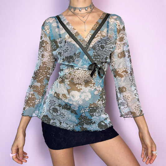 The Y2K Floral Mesh Wrap Top is a dreamy vintage 2000s piece made from semi-sheer stretch mesh in a soft white base with delicate floral print in tones of blue and brown. Designed with a flattering wrap silhouette, it features slightly flared 3/4 sleeves with side slits, adding movement and a romantic touch. Lightweight and breathable — perfect for layering, summer outfits, festival looks, or casual styling. Excellent vintage condition. adult world shop
