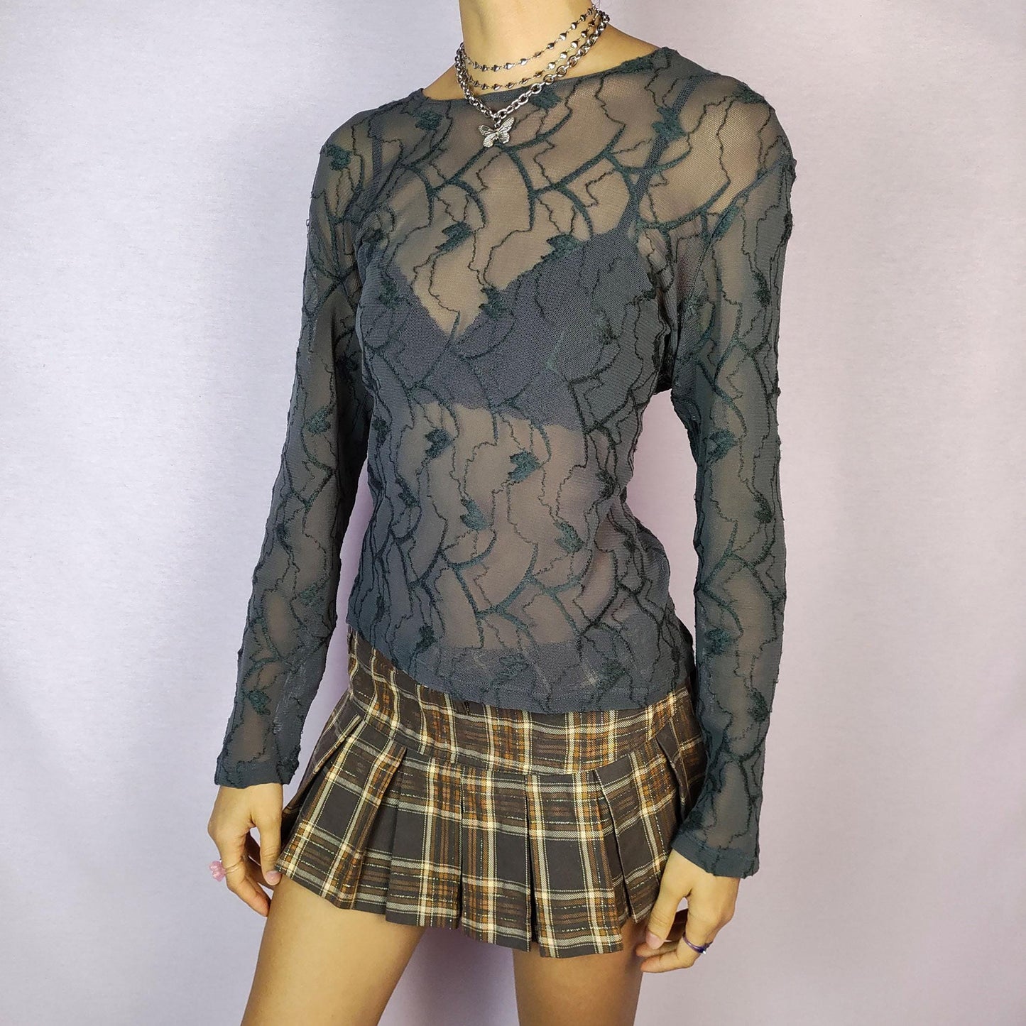 The Y2K Gray Sheer Mesh Top is a vintage 2000s piece featuring a semi-sheer design with intricate textured patterns. Crafted from soft, lightweight mesh fabric, it has a slim-fit silhouette with long sleeves, making it perfect for layering