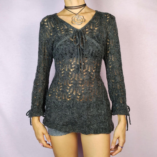 The Y2K Gray Sheer Sweater is a vintage 2000s pullover featuring a delicate knit pattern with semi-sheer details, offering a lightweight yet cozy feel. Designed with three quarter sleeves and a tie detail at the neckline, this sweater