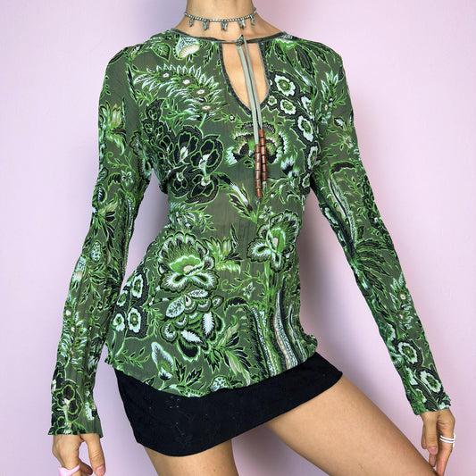 The Y2K Green Boho Tie Front Top is a vintage 2000s piece featuring an abstract floral print on lightweight, semi-sheer fabric. Designed with a front keyhole neckline and adjustable tie adorned with wooden bead details. The long sleeves and breathable material make it comfy and flattering. A unique top perfect for summer layering, festival outfits, fairy grunge, or earthy boho styles.