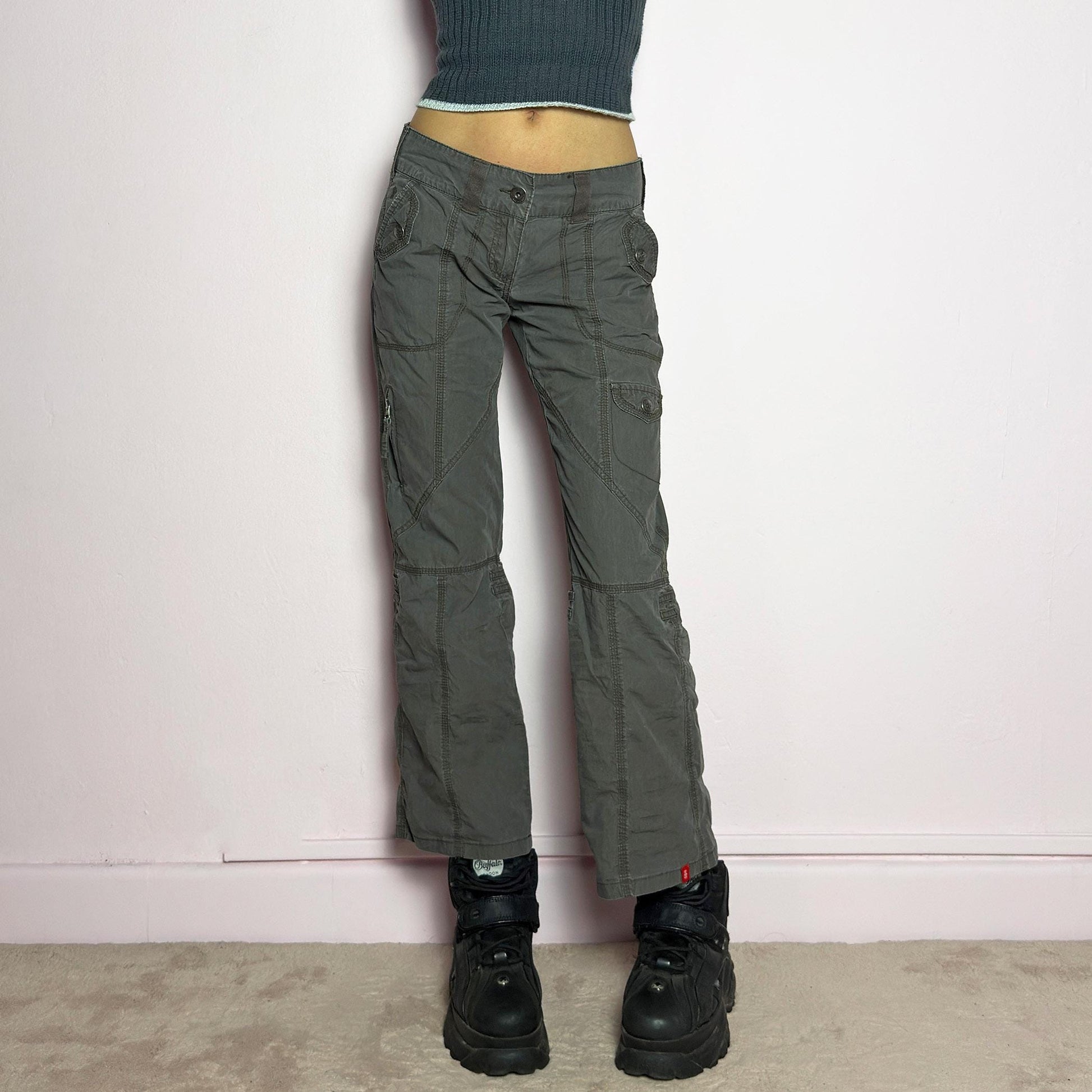 The Y2K Low-Rise Cargo Pants are a vintage 2000s piece featuring a washed gray tone with contrast stitching. Designed with a low-rise fit, button and zipper closure, and multiple cargo-style pockets, these pants have panel detailing and exposed seams that enhance their utilitarian aesthetic. The cropped straight-leg cut adds a modern touch, making them perfect for grunge and streetwear-inspired outfits. adult world shop