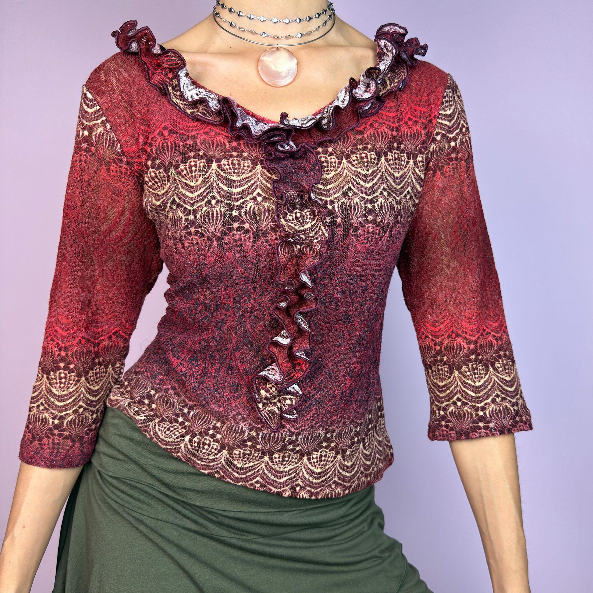 The Y2K Maroon Ruffle Mesh Top is a romantic vintage 2000s piece. Featuring a semi-sheer lace-inspired design in warm red tones, it showcases intricate patterns complemented by a ruffled neckline and 3/4 sleeves. adult world shop