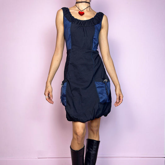 The Y2K Navy & Black Bubble Mini Dress is a bold vintage 2000s statement piece with utility-inspired vibes. Features a unique bubble hem, ruched scoop neckline, and structured paneled design with contrast navy inserts. Equipped with chunky side pockets and metal ring details for an industrial touch. Made from a stretchy fabric with a techy texture. Perfect for dystopian streetwear, cyber grunge, or Harajuku styling. Great vintage condition.