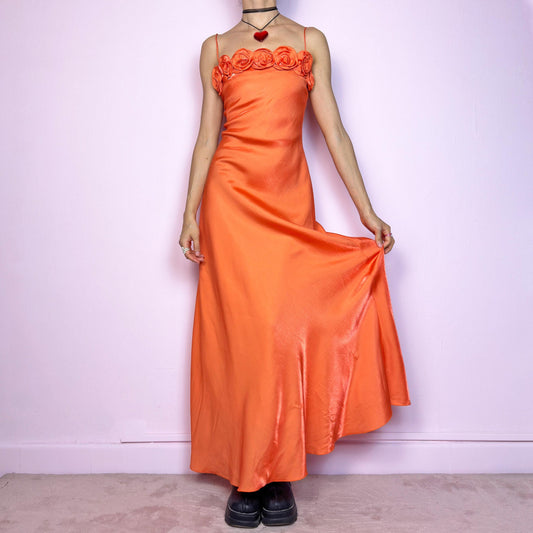 The Y2K Orange Rose Maxi Dress is a stunning 2000s satin-style slip dress featuring a vibrant orange tone and romantic rose appliqué details along the bust. Designed with skinny spaghetti straps and a softly flared maxi silhouette that drapes beautifully. Lightweight and glossy with a smooth sheen – a perfect statement piece for summer weddings, garden parties, or dreamy fairycore evenings. Made in France.