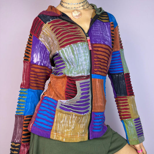 The Y2K Patchwork Hoodie is a vintage 2000s playful hippie sweater featuring a patchwork design with vibrant, hand-sewn panels in earthy and jewel tones. It includes a front zipper, a cozy hood, kangaroo pockets. adult world shop