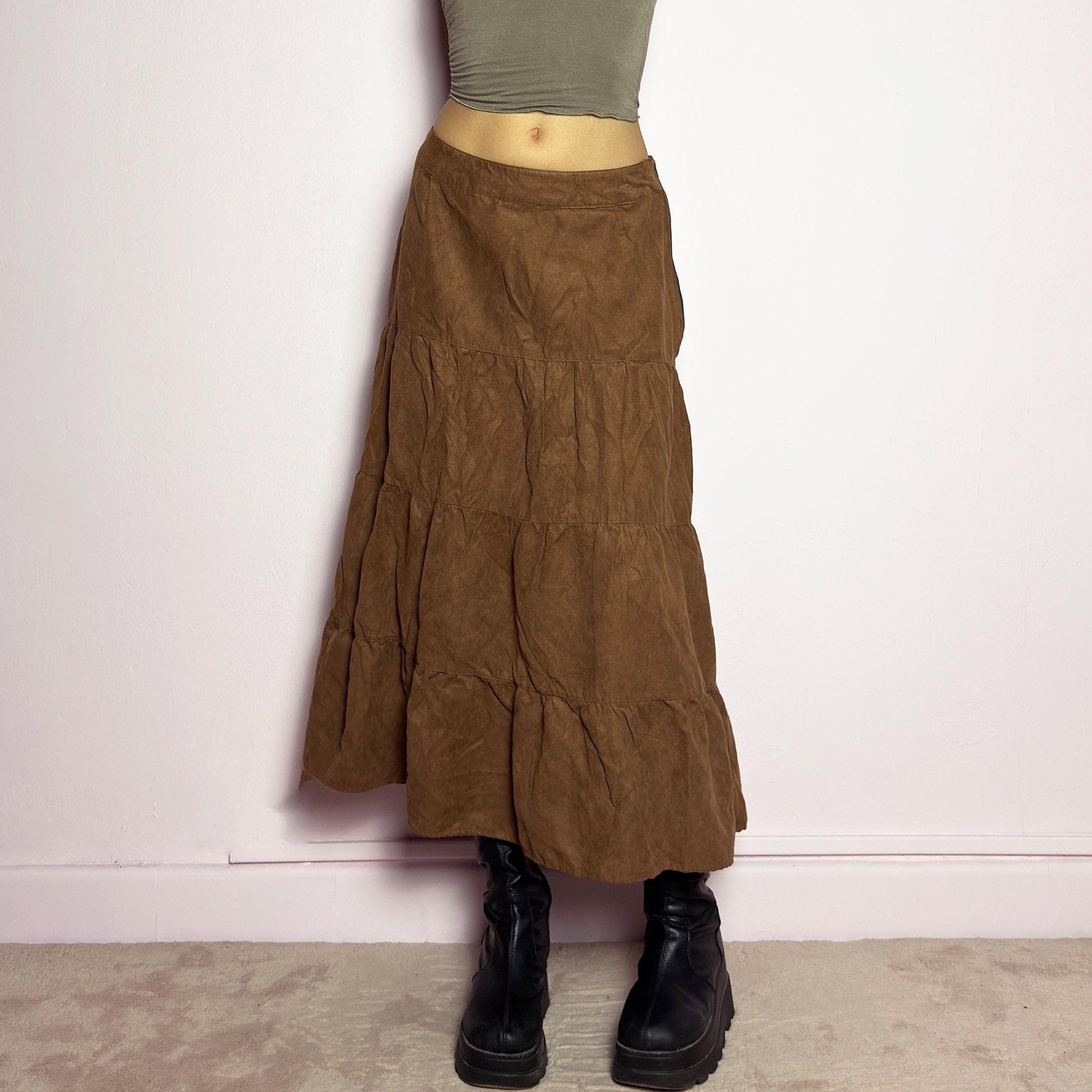 The Y2K Tiered Brown Midi Skirt is a vintage 2000s piece featuring a soft faux suede style fabric. Designed with a voluminous tiered structure for a flowy silhouette and a side zipper closure, this skirt has a mid-rise fit and an earthy brown tone, perfect for bohemian or casual outfits. adult world shop