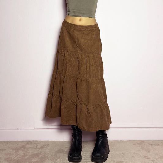The Y2K Tiered Brown Midi Skirt is a vintage 2000s piece featuring a soft faux suede style fabric. Designed with a voluminous tiered structure for a flowy silhouette and a side zipper closure, this skirt has a mid-rise fit and an earthy brown tone, perfect for bohemian or casual outfits. adult world shop