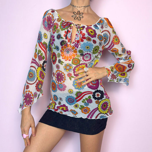 The Y2K White Floral Tie Front Top is a vintage 2000s piece bursting with color and retro charm. Features a vibrant multicolor 60s-inspired flower print on lightweight, slightly sheer pleated fabric. Designed with a flattering scoop neckline, keyhole front with tie closure, and flared bell sleeves. Stretchy and breathable – perfect for summer, festivals, or hippie styles. Great vintage condition.