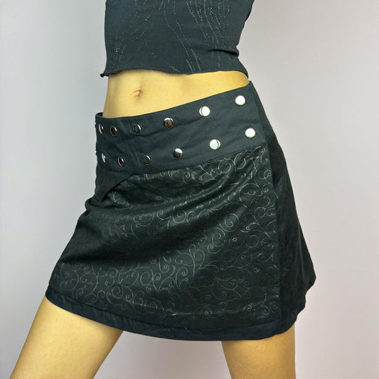 The Y2K Wrap Mini Black Skirt is a vintage 2000s piece featuring a snap-button closure on the waistband for an adjustable fit. Made from a thick fabric with a subtle floral pattern design, its wrap silhouette. adult world shop