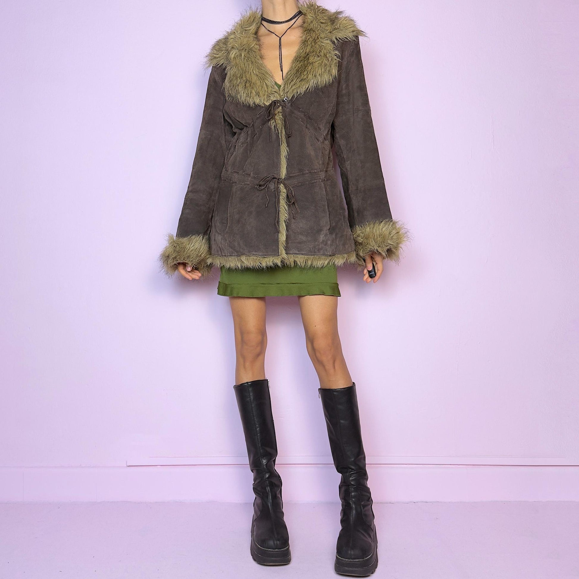 The Vintage 90s Brown Suede Penny Lane Jacket features a brown leather suede exterior and plush faux fur trim on the collar, cuffs, and hemline. Featuring tie-front closures for a snug fit and a flattering silhouette
