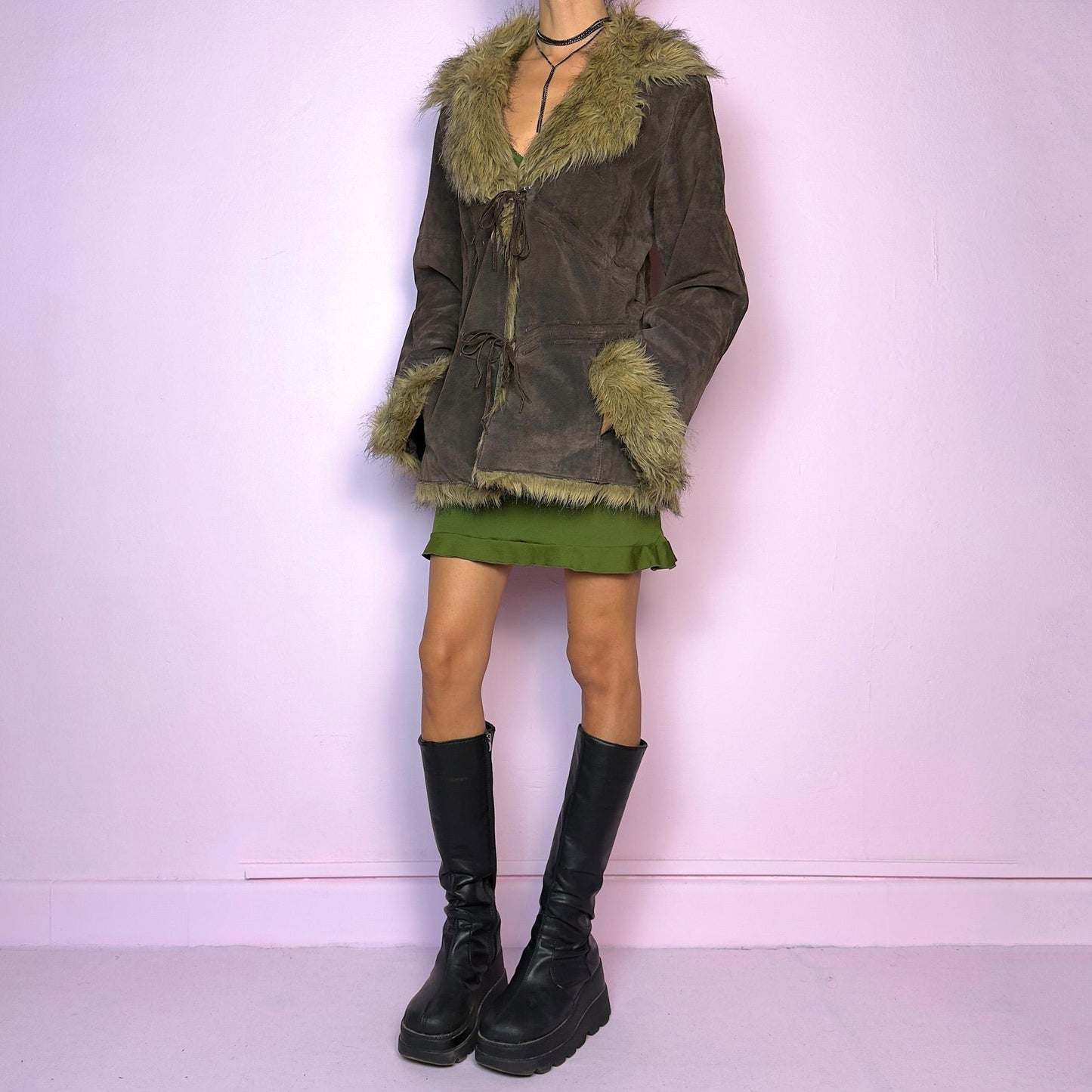 The Vintage 90s Brown Suede Penny Lane Jacket features a brown leather suede exterior and plush faux fur trim on the collar, cuffs, and hemline. Featuring tie-front closures for a snug fit and a flattering silhouette