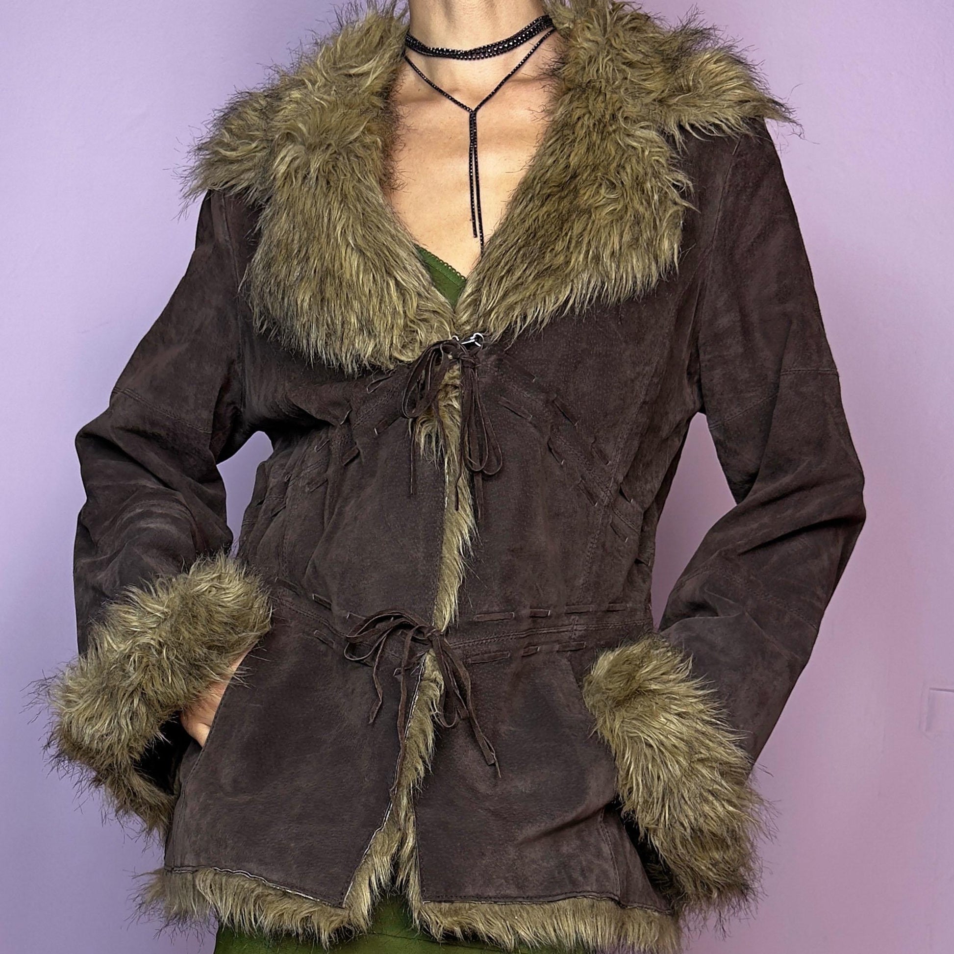 The Vintage 90s Brown Suede Penny Lane Jacket features a brown leather suede exterior and plush faux fur trim on the collar, cuffs, and hemline. Featuring tie-front closures for a snug fit and a flattering silhouette