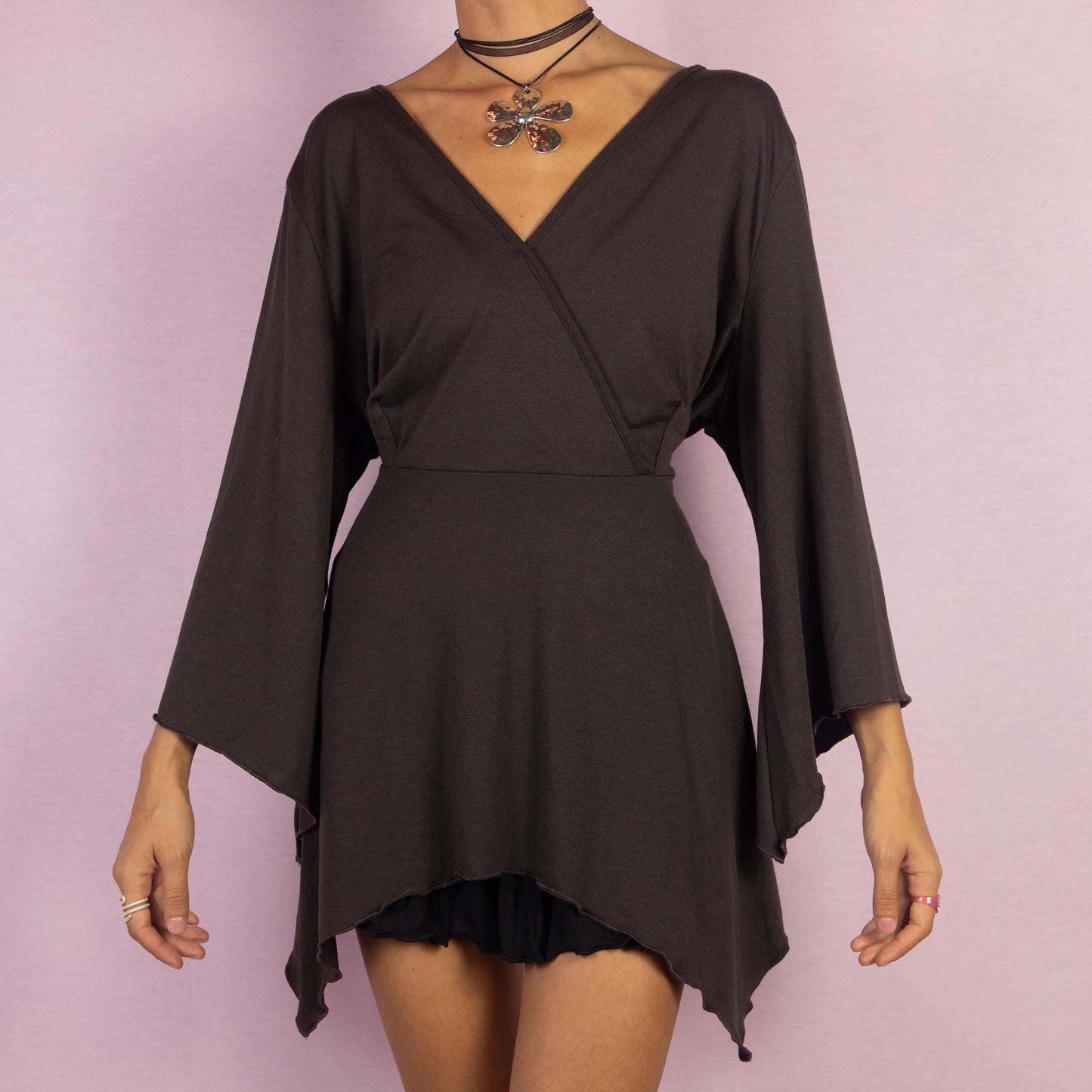 The Y2K Brown Bell Sleeve Top is a whimsical vintage 2000s blouse featuring a deep V-neckline and dramatic bell sleeves that enhance its enchanting boho-inspired aesthetic. The asymmetrical hem adds a unique, flowy silhouette.