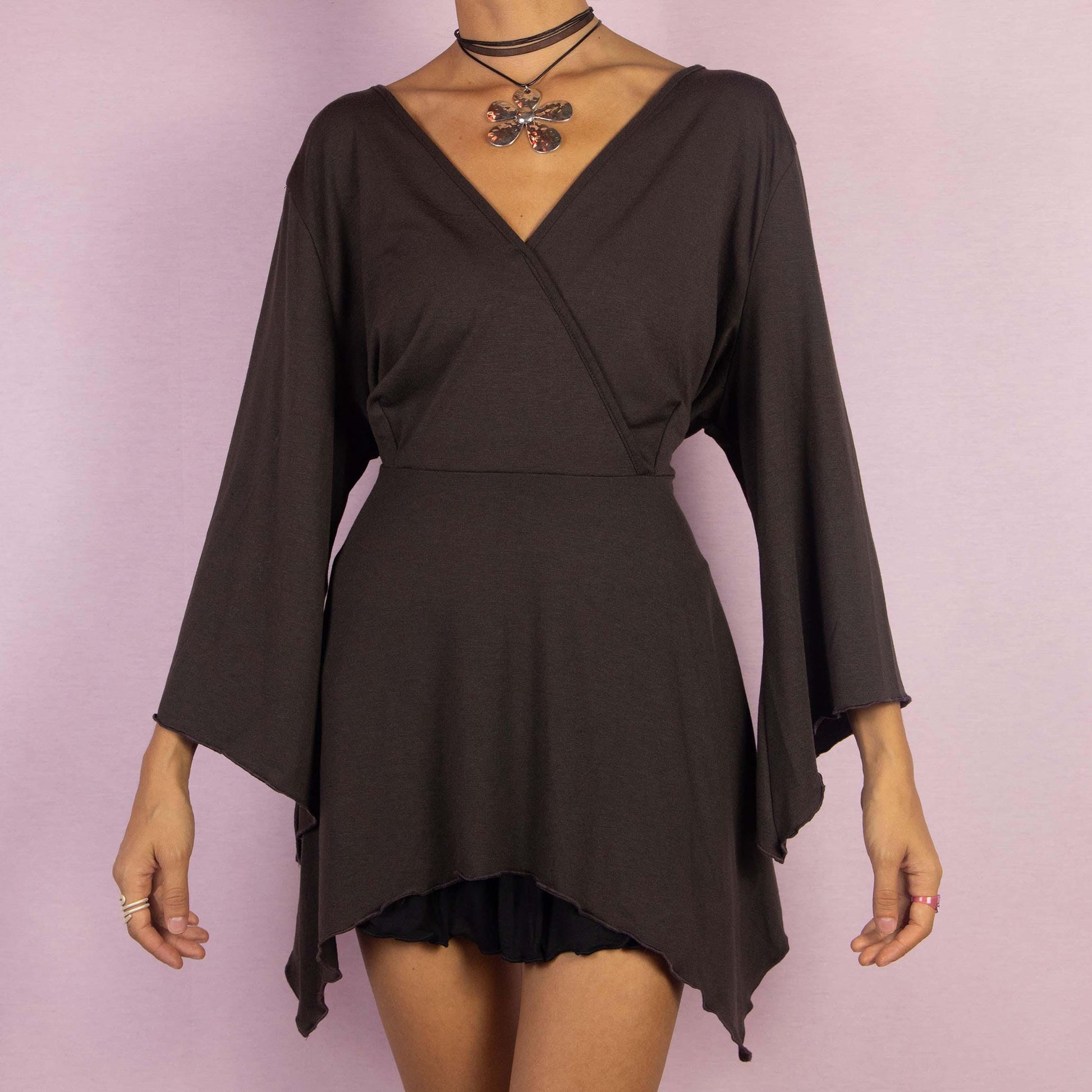 The Y2K Brown Bell Sleeve Top is a whimsical vintage 2000s blouse featuring a deep V-neckline and dramatic bell sleeves that enhance its enchanting boho-inspired aesthetic. The asymmetrical hem adds a unique, flowy silhouette.