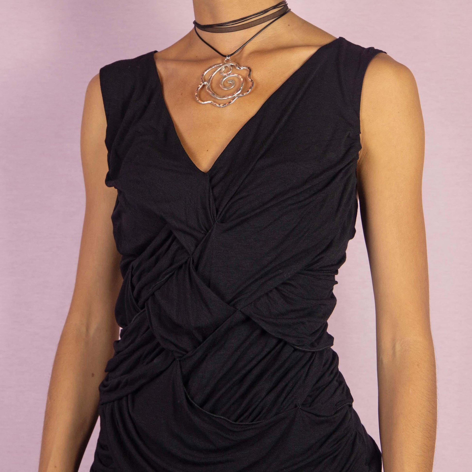 The Y2K Black Ruched Draped Top is a vintage 2000s sleeveless shirt featuring a ruched and draped design with woven detailing at the front. Its fitted silhouette and deep V-neckline create a sleek and edgy look, perfect for evening outings