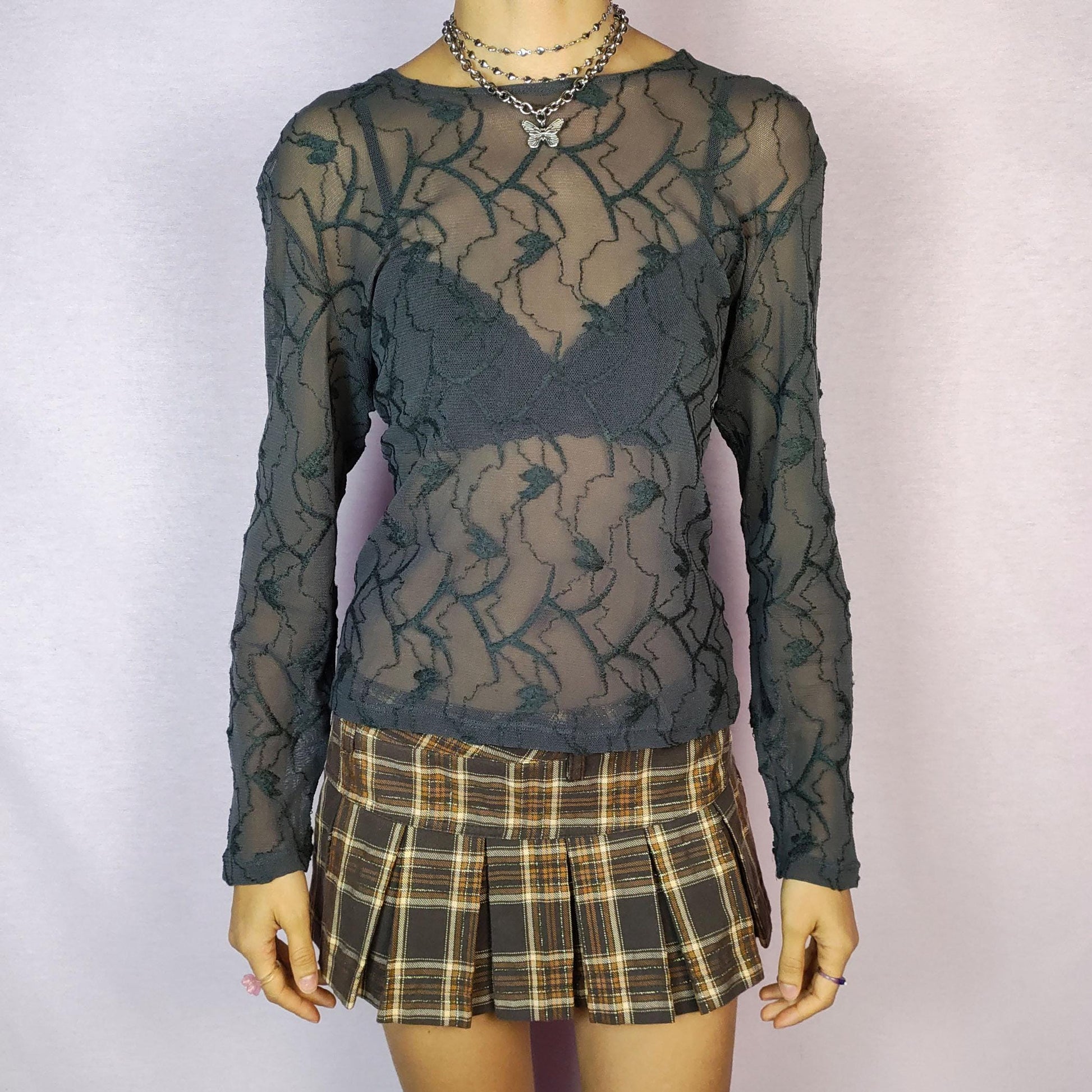 The Y2K Gray Sheer Mesh Top is a vintage 2000s piece featuring a semi-sheer design with intricate textured patterns. Crafted from soft, lightweight mesh fabric, it has a slim-fit silhouette with long sleeves, making it perfect for layering