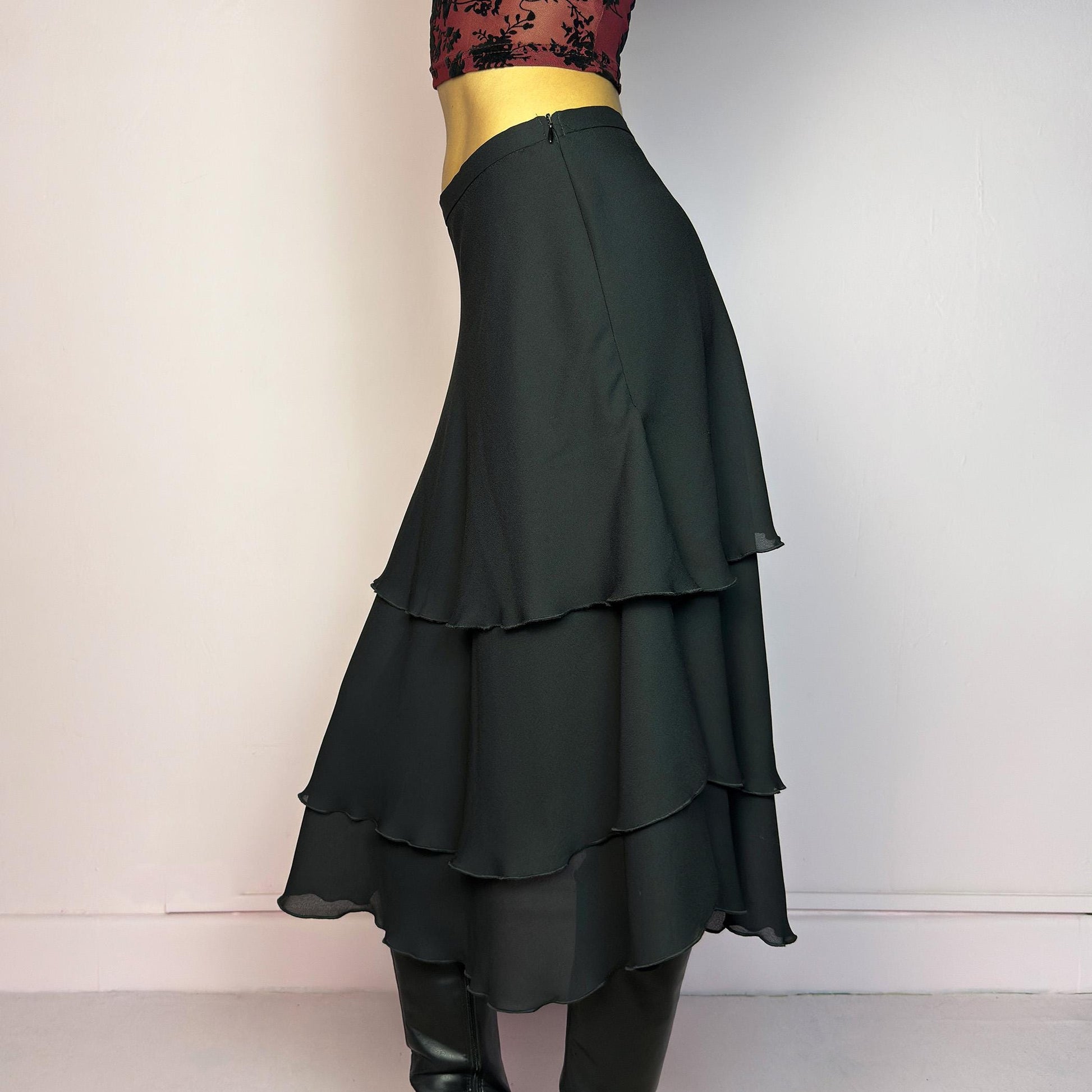 The Vintage 90s Black Layered Tiered Skirt features a flowy, tiered design with cascading chiffon-like layers. It includes a side zipper closure. Its versatile length and elegant style make it perfect for evening parties. Adult World Shop