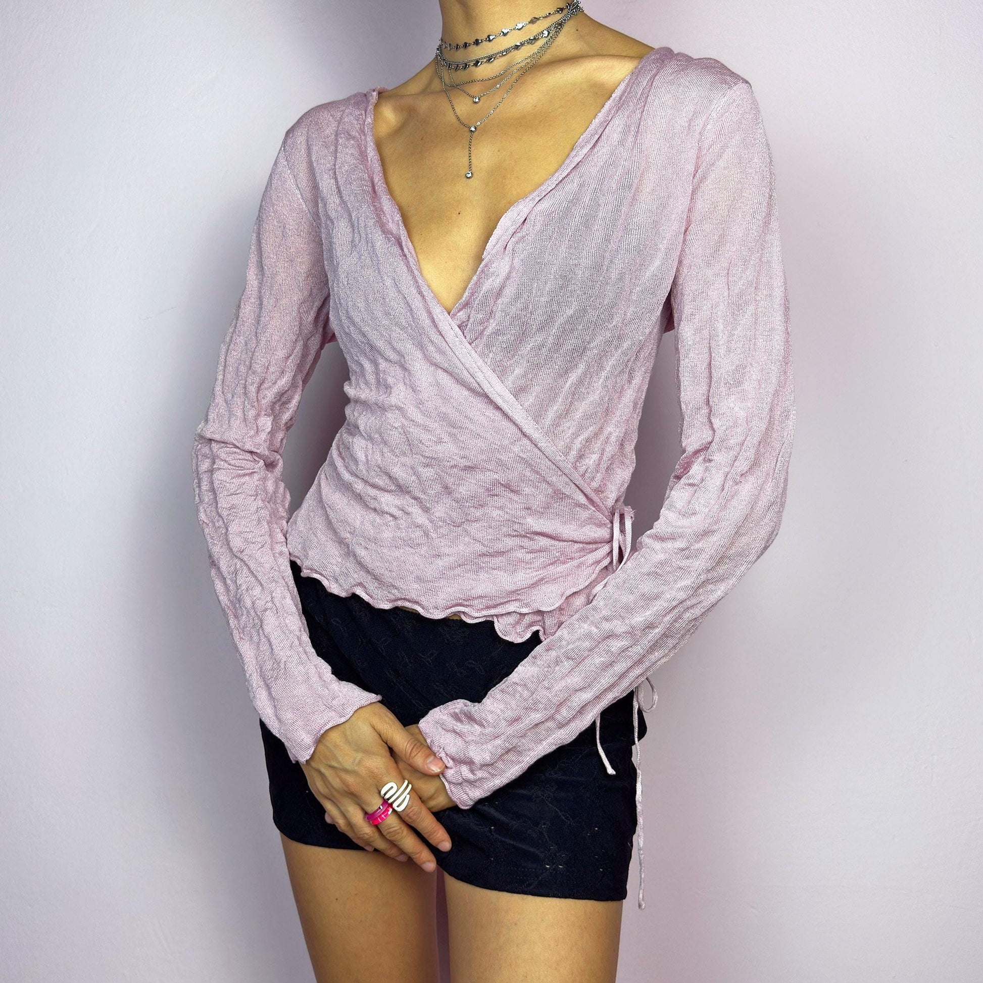 The Y2K Pink Wrap Tie Cardigan is a vintage 2000s delicate and feminine piece featuring a light pink hue and a textured knit fabric. Its wrap-around design ties at the side, creating an adjustable and flattering fit. adult world shop