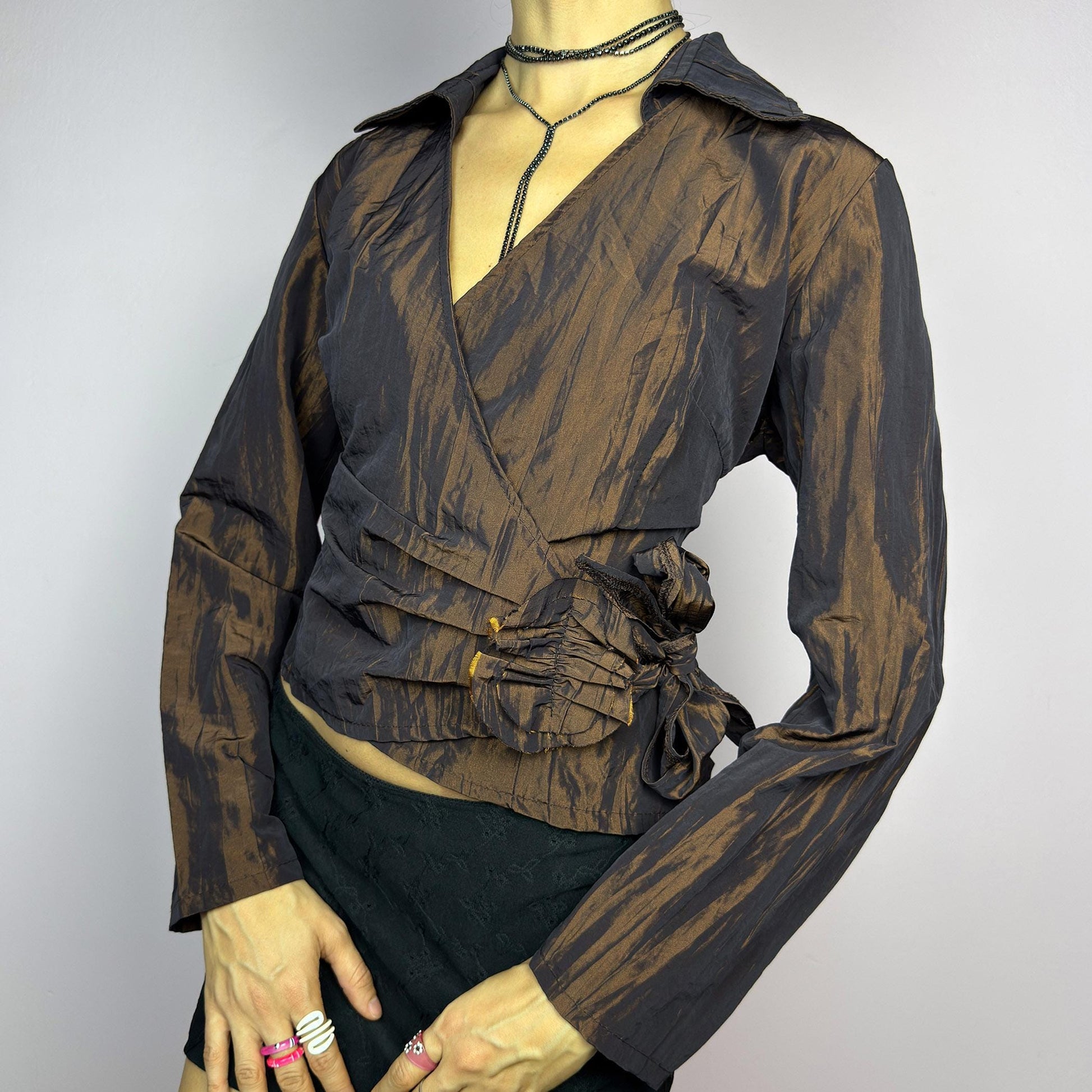 The Vintage 90s Brown Wrap Tie Blouse features a textured, crinkled fabric with a subtle iridescent finish, a flattering wrap design with a tie at the side. The deep brown tone adds versatility, while the structured collar. adult world shop