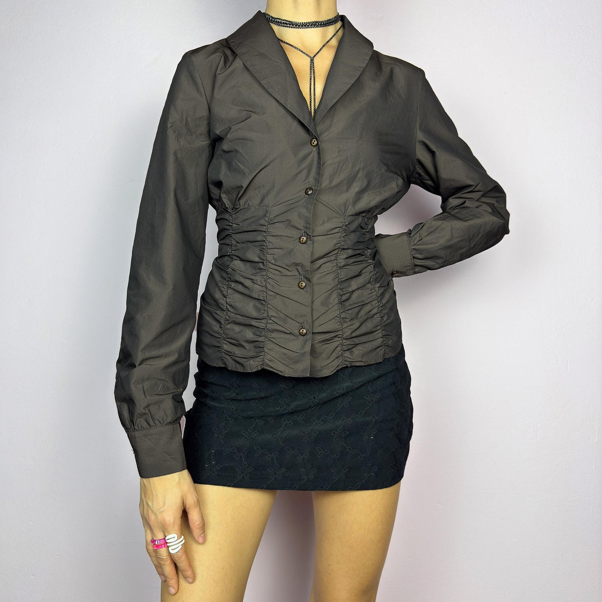 The Vintage 90s Brown Ruched Blouse features a structured yet feminine design with ruched detailing on both the front and back, creating a flattering silhouette. Crafted in a deep brown tone, it includes a tailored collar. adult world shop