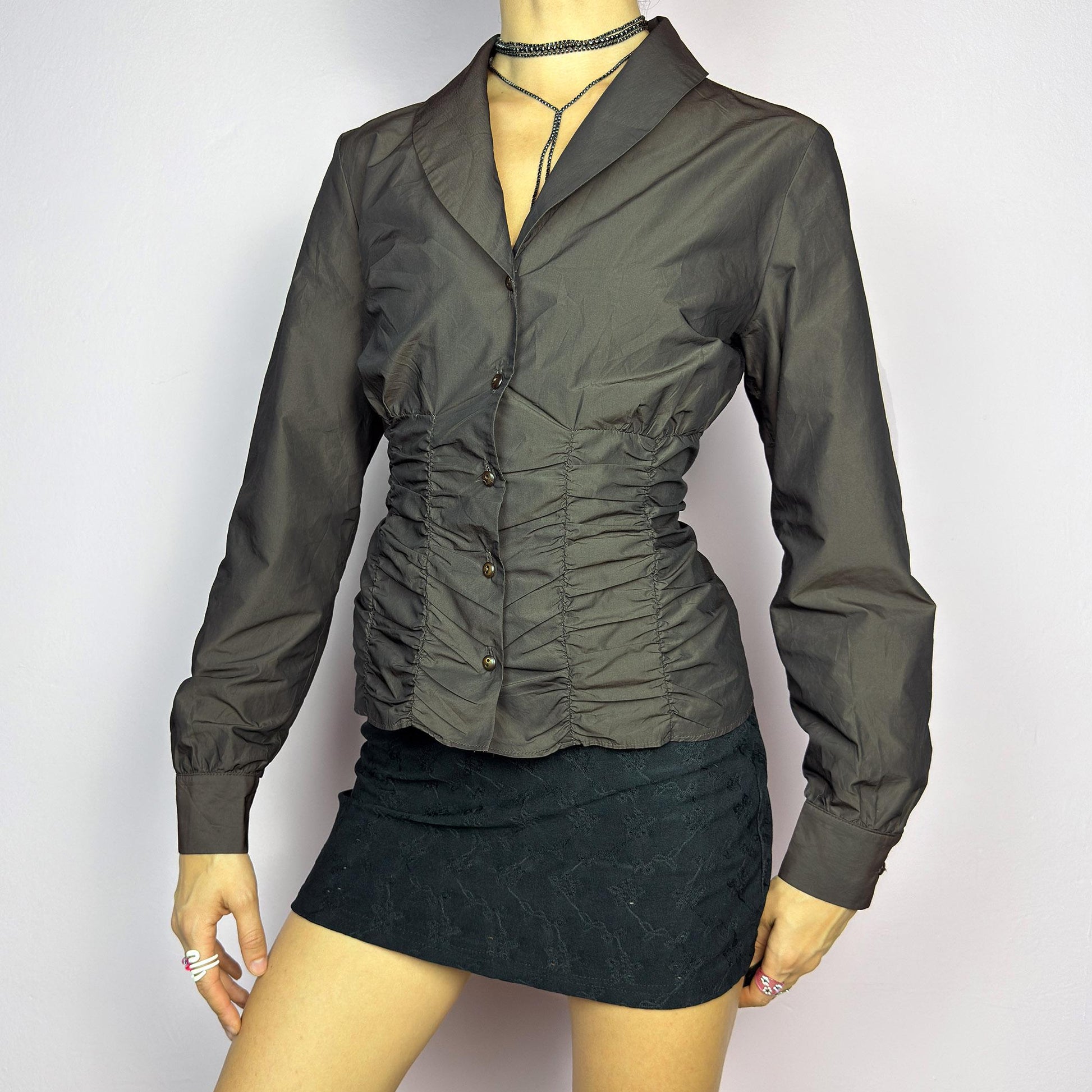 The Vintage 90s Brown Ruched Blouse features a structured yet feminine design with ruched detailing on both the front and back, creating a flattering silhouette. Crafted in a deep brown tone, it includes a tailored collar. adult world shop