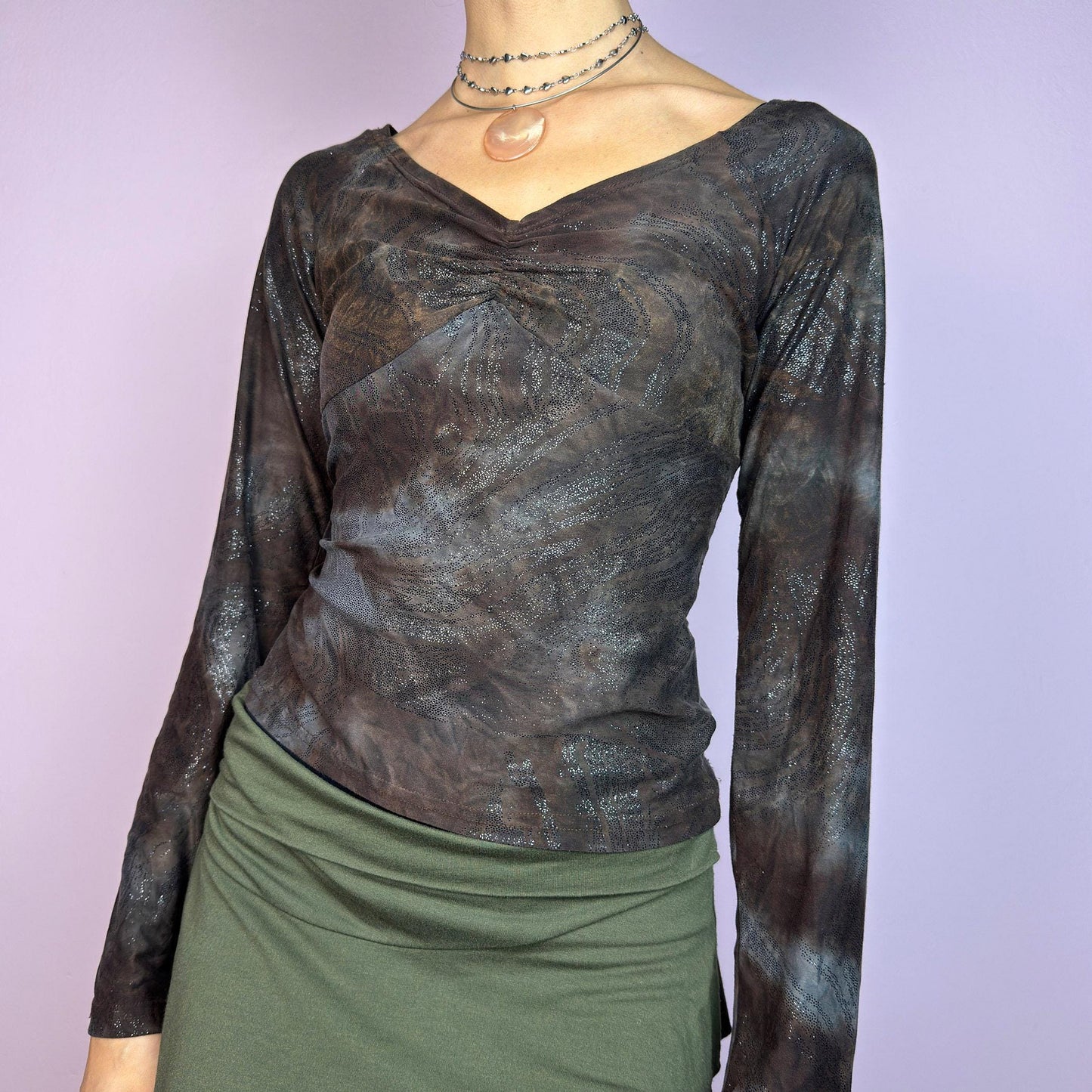 The Y2K Brown Earthy Shimmer Top is a vintage 2000s fitted and stretchy long-sleeve blouse with an earthy, abstract pattern featuring a ruched detail at the bust and subtle shimmering accents throughout. Perfect for casual outings. adult world shop